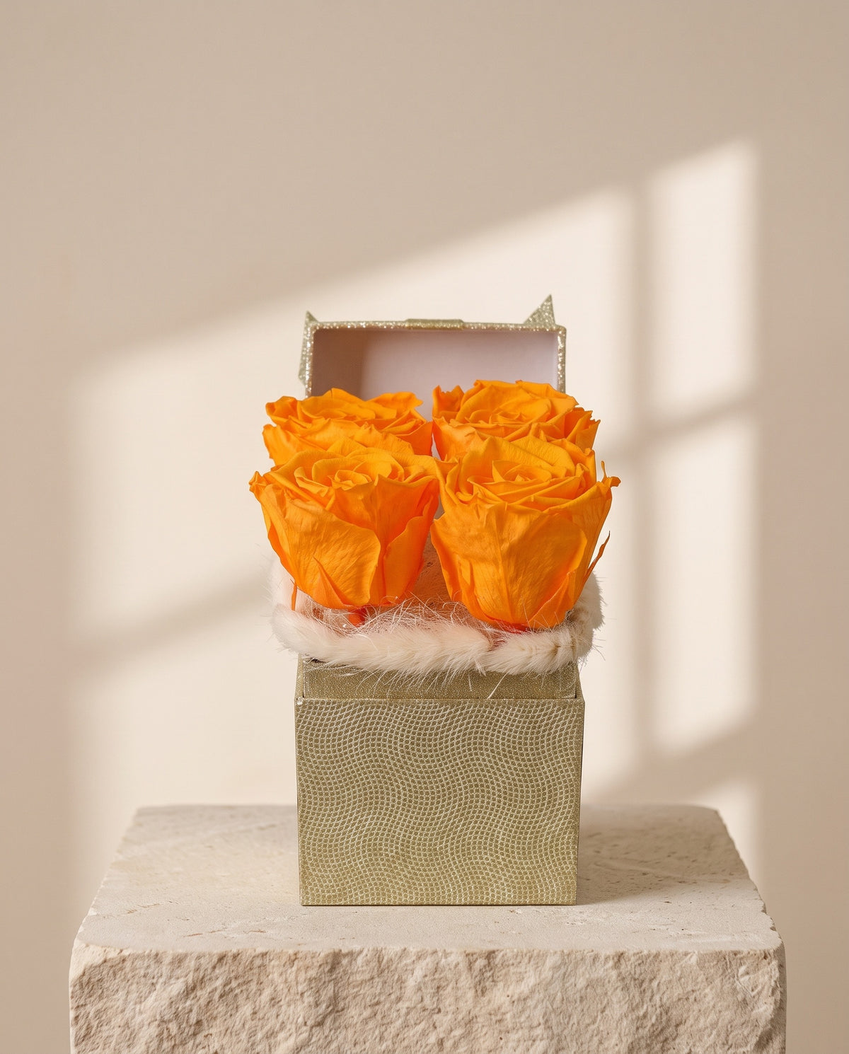 Centro de flores preservadas en naranja, con su recipiente, sobre fondo crema.