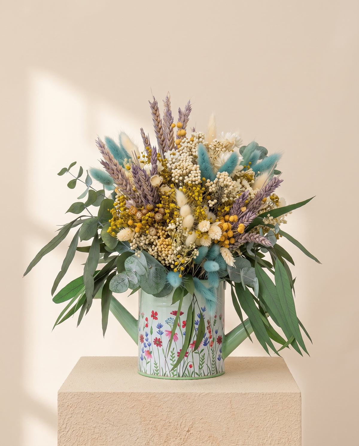 Centro de flores secas y preservadas en azul y crema, con su recipiente, sobre fondo crema.