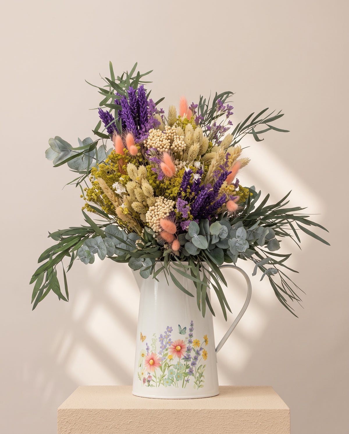 Centro de flores secas y preservadas en lavanda y amarillo, con su recipiente, sobre fondo crema.