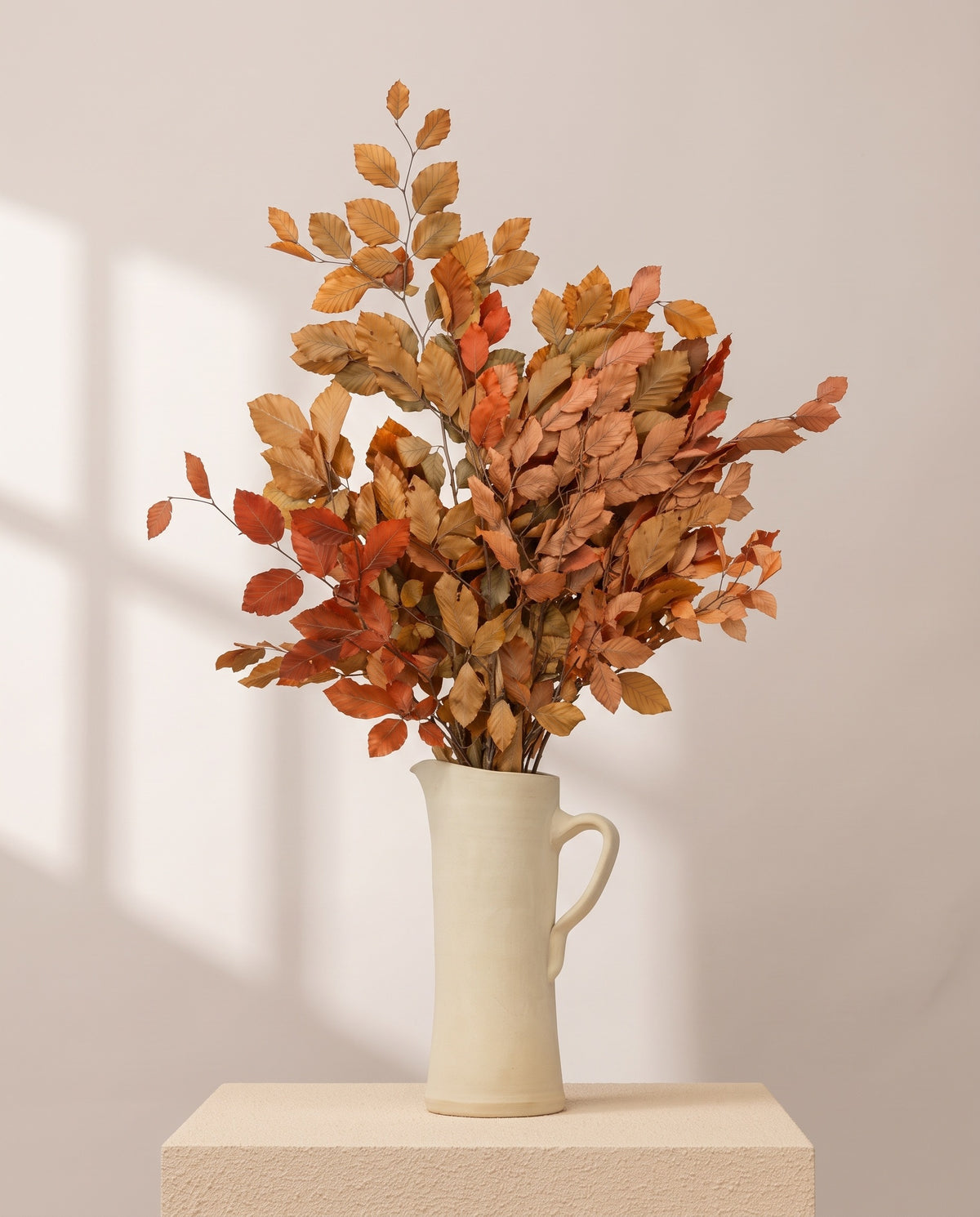 Faia preservada vermelha e laranja numa jarra de cerâmica creme, em ambiente decorado. Jarra não incluída.