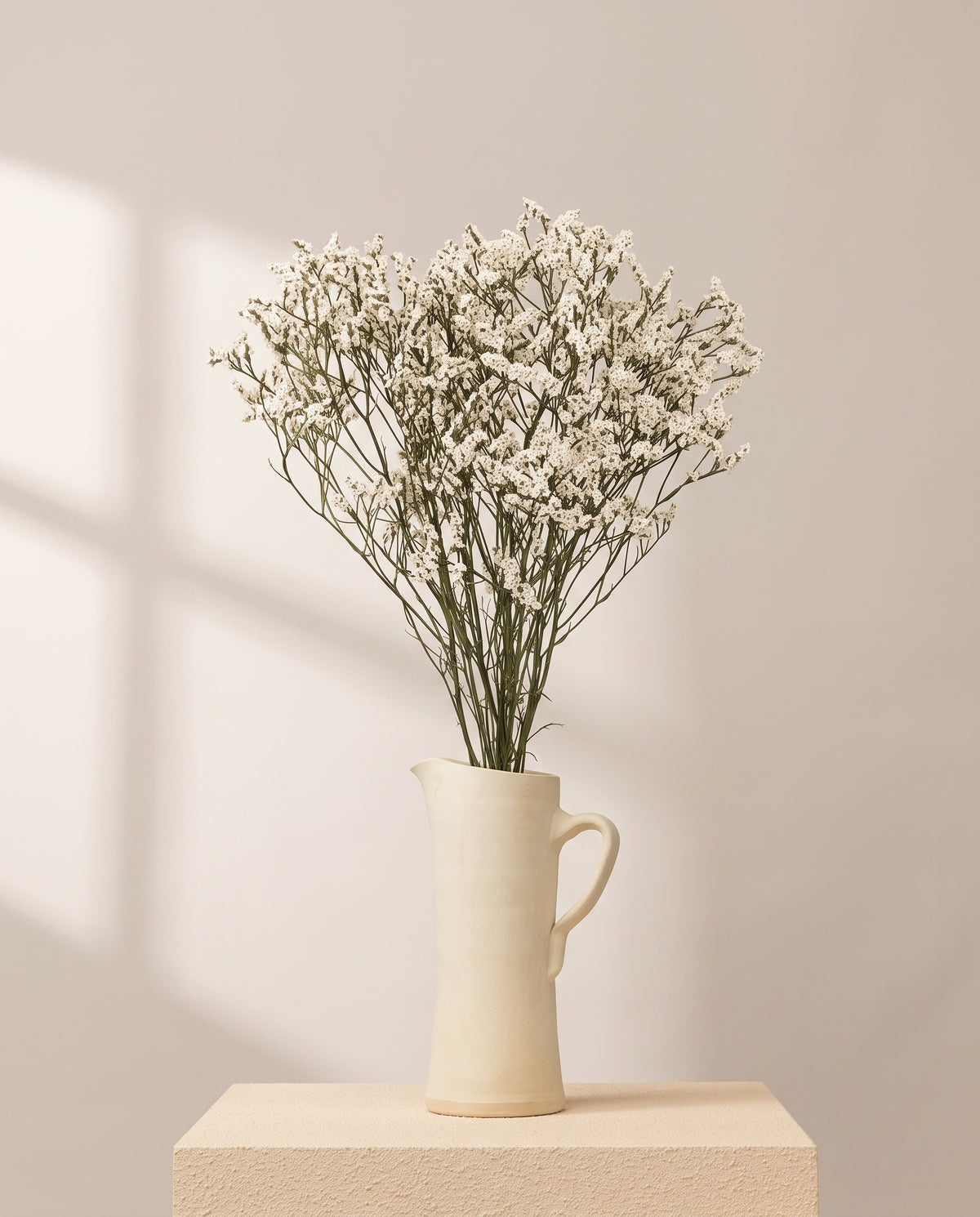 Limonium Sinensis preservado blanco en una jarra de cerámica crema. Jarra no incluida.
