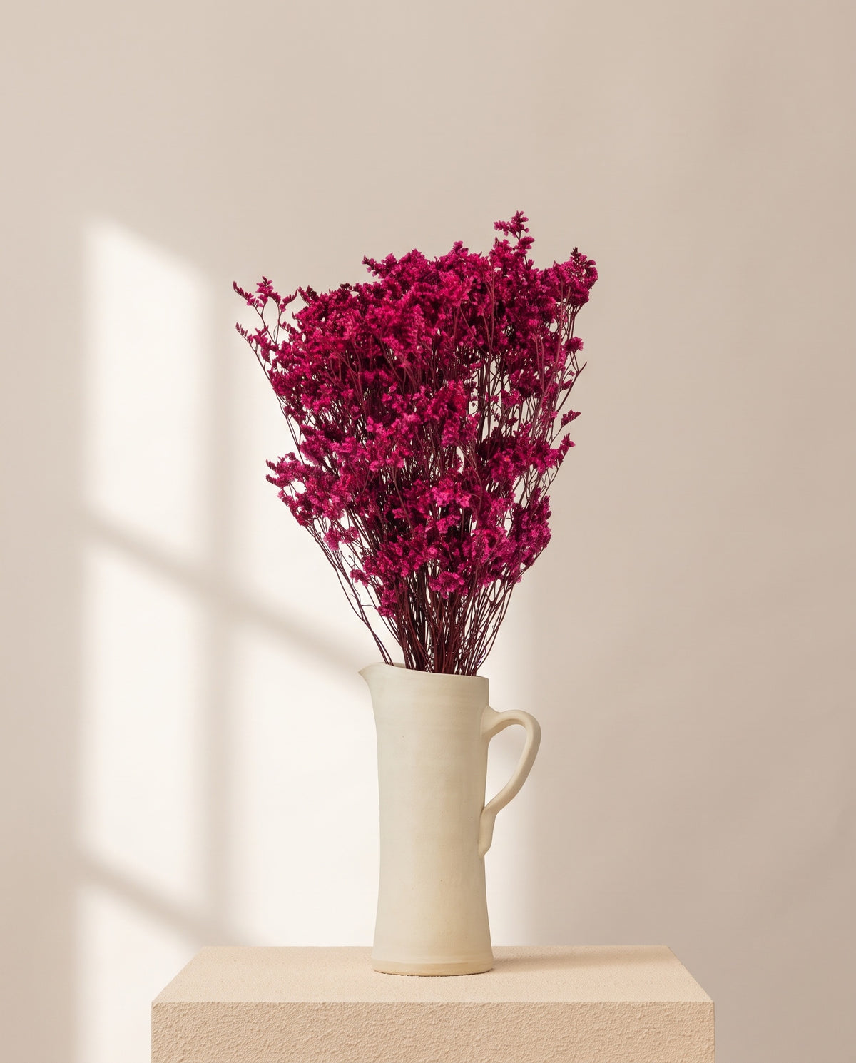Limonium Sinensis preservado fucsia en una jarra de cerámica crema. Jarra no incluida.