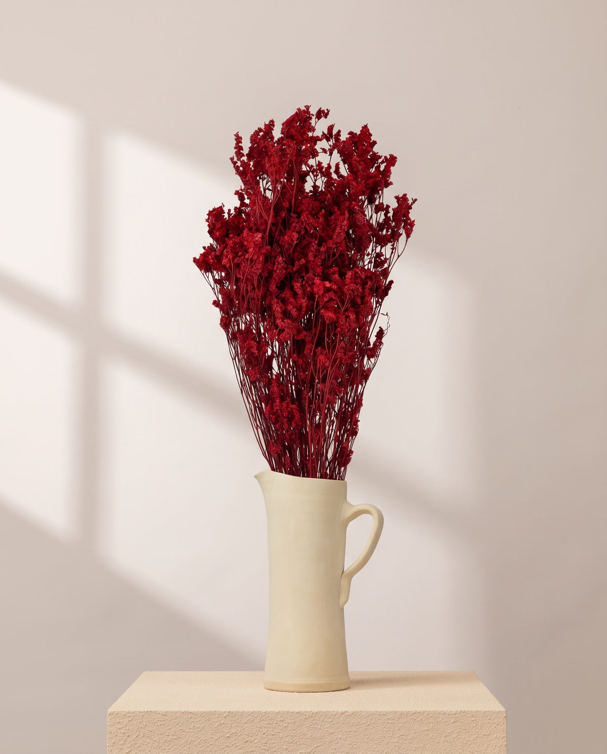 Limonium Sinensis preservado rojo en una jarra de cerámica crema. Jarra no incluida.