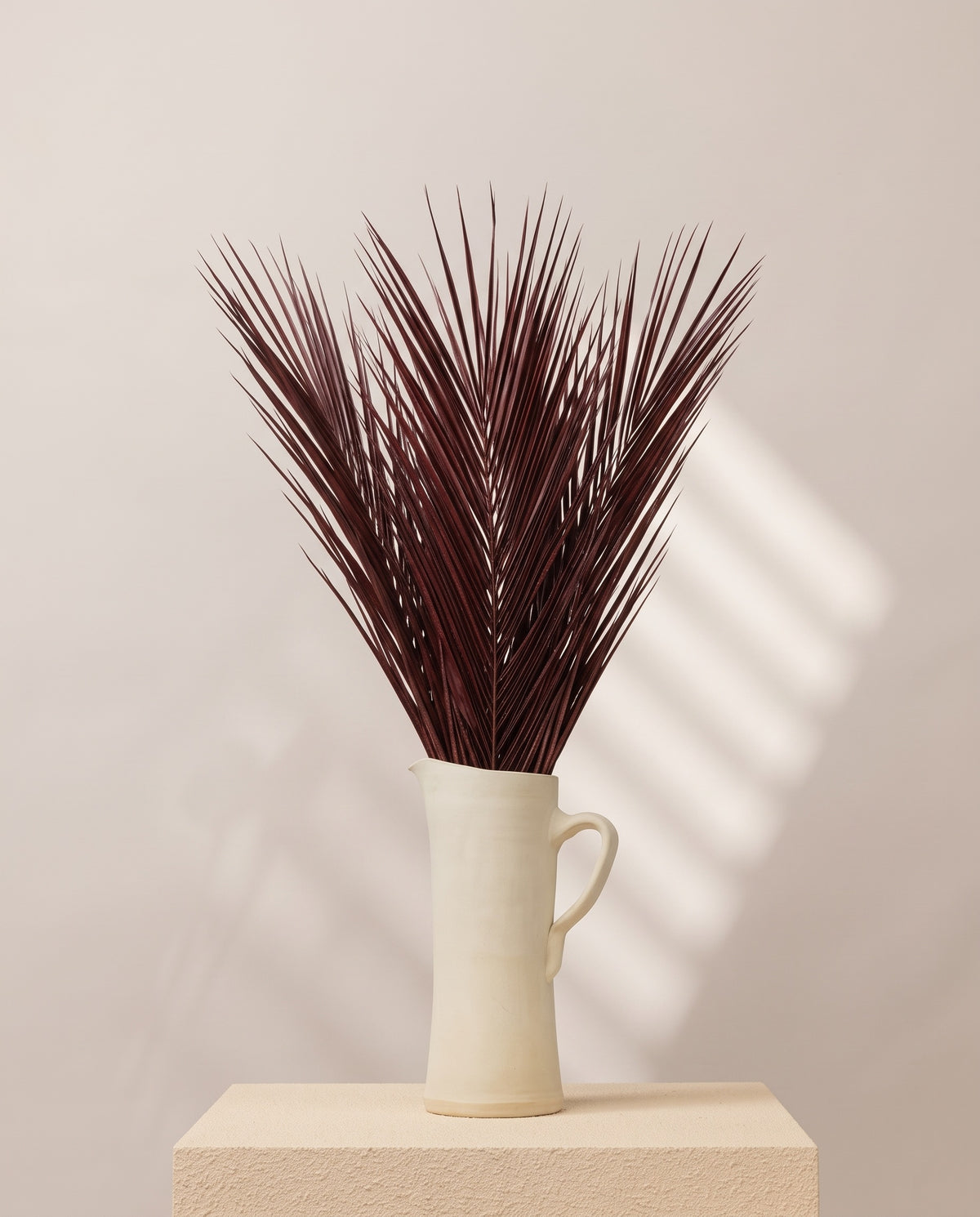 Palmeira robellini preservada grená numa jarra de cerâmica creme, em ambiente decorado. Jarra não incluída.