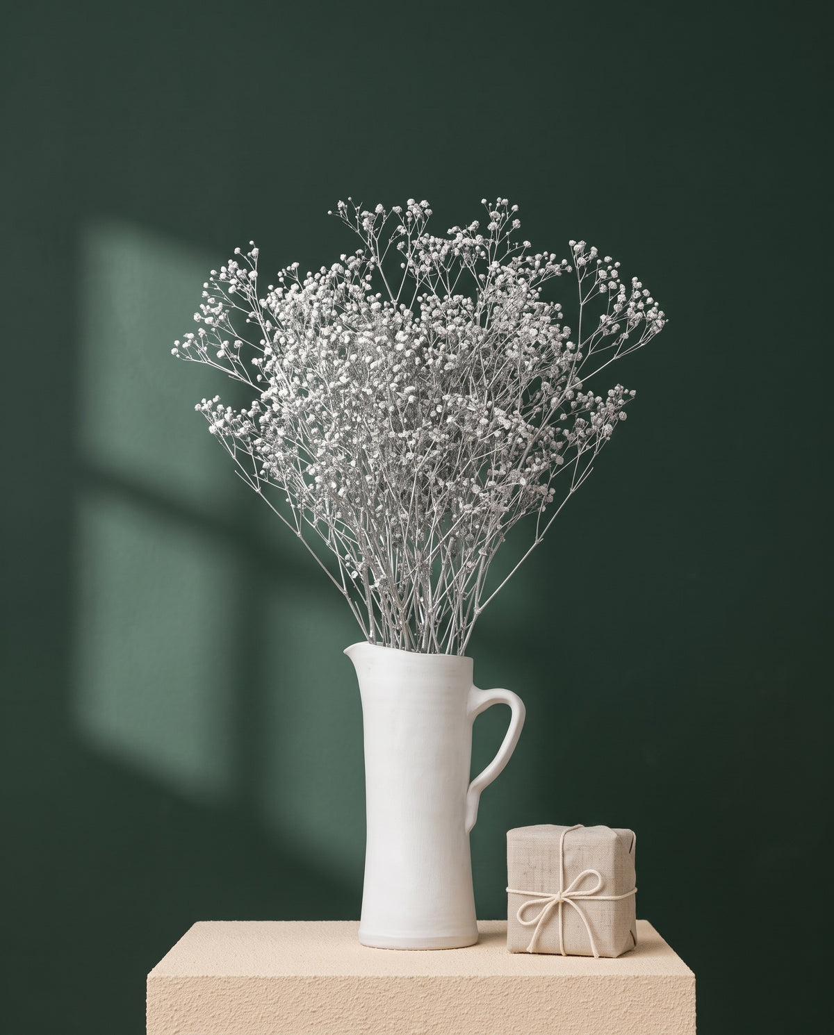 Mazo de paniculata mini preservada plateada en jarra de cerámica blanca, con caja regalo de lino y pared verde bosque. Jarra y caja no incluidas.