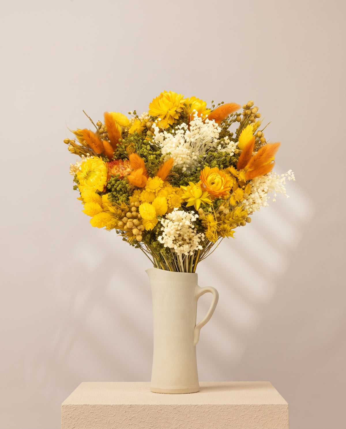 Ramo de flores secas em amarelo numa jarra de cerâmica creme. Jarra não incluída.