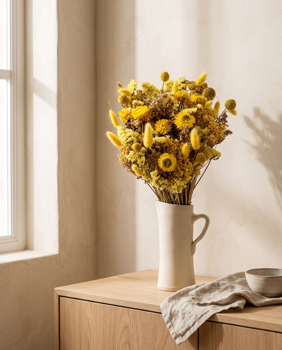 Ramo de flores secas en amarillo en una jarra sobre un aparador, ambiente de casa. Jarra no incluida.
