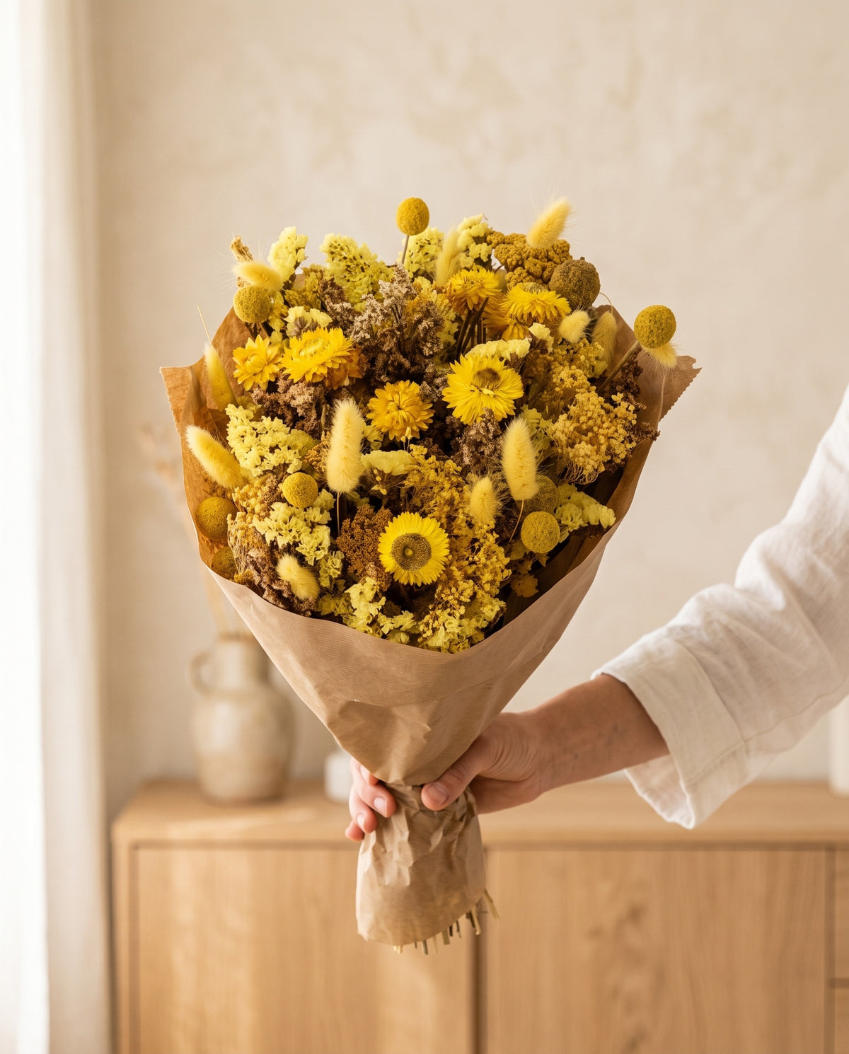 Mano sujetando el ramo de flores secas en amarillo con su papel, como se entrega.