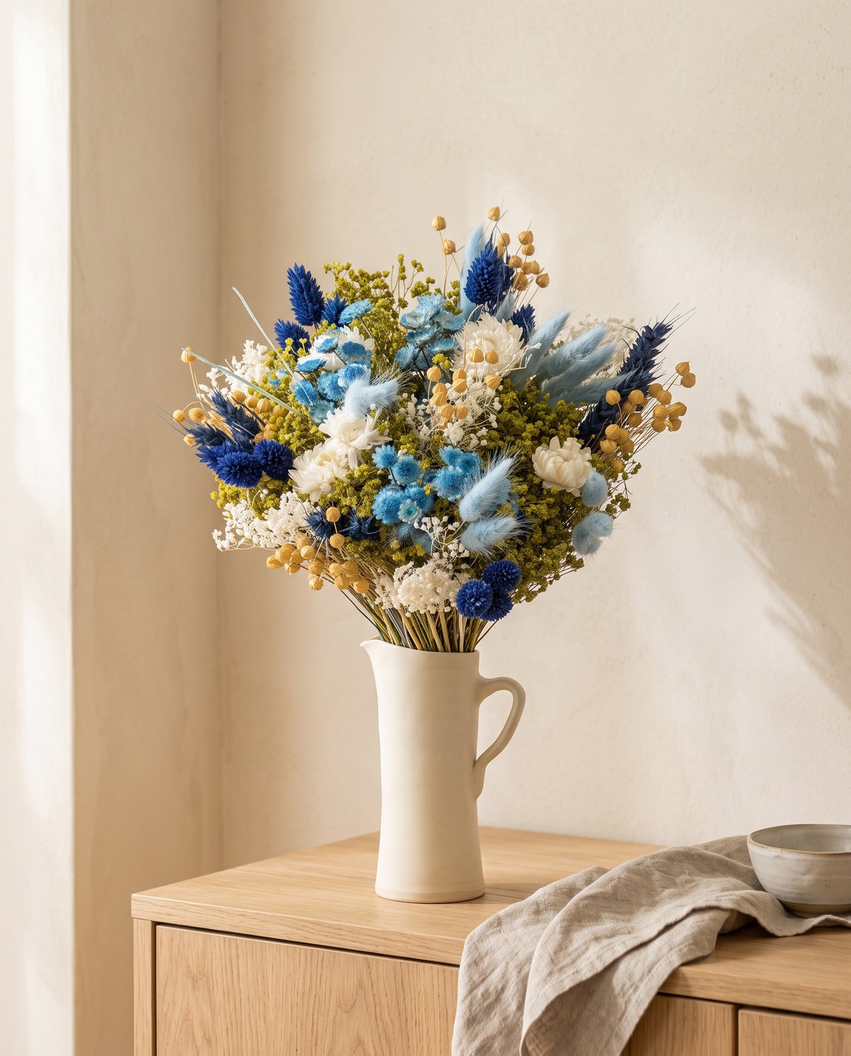 Ramo de flores secas em azul numa jarra sobre um aparador, ambiente de casa. Jarra não incluída.