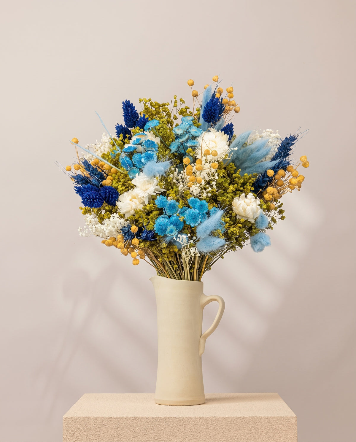 Ramo de flores secas em azul numa jarra de cerâmica creme. Jarra não incluída.