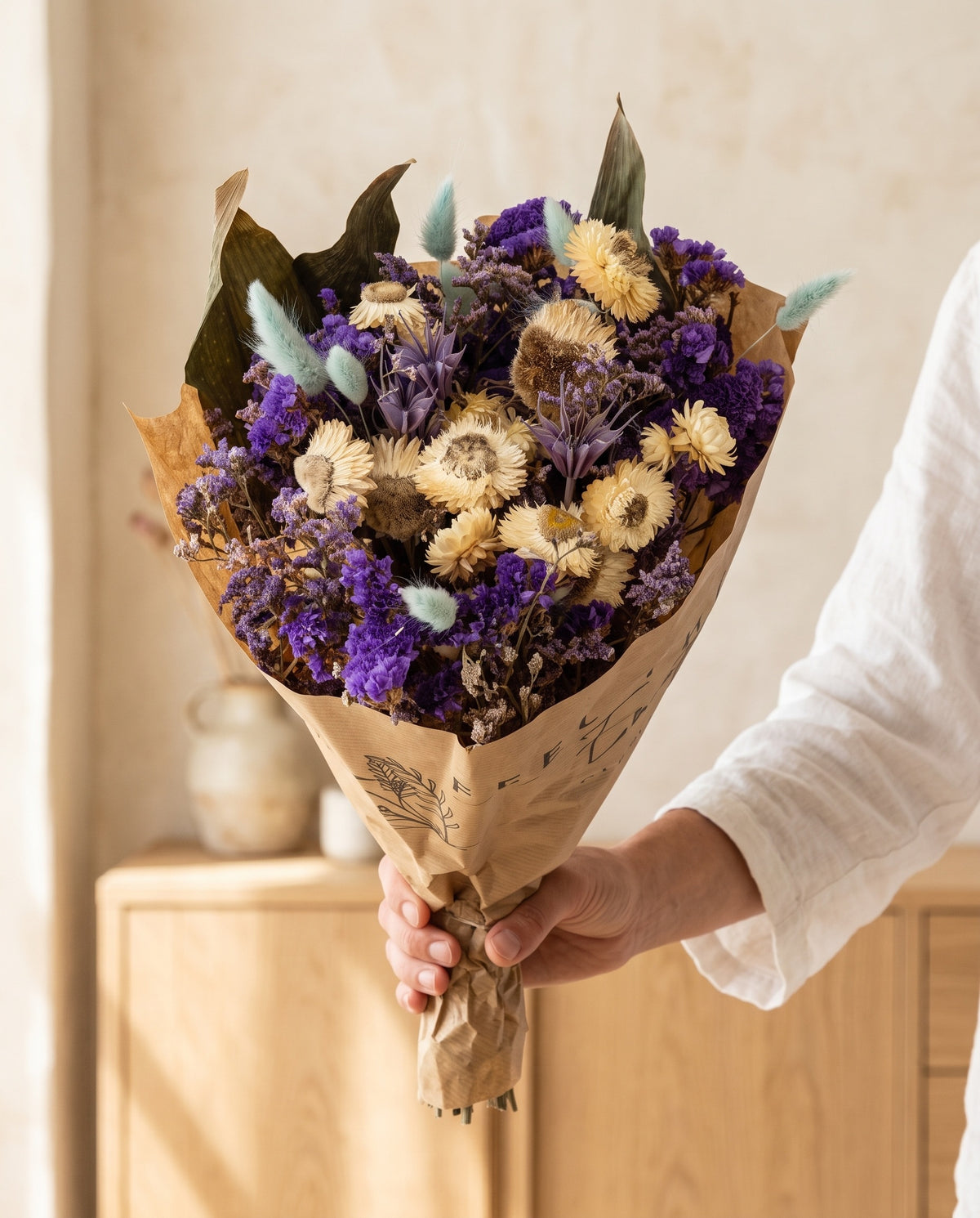 Mano sujetando el ramo grande de flores secas en azul con su papel, como se entrega.
