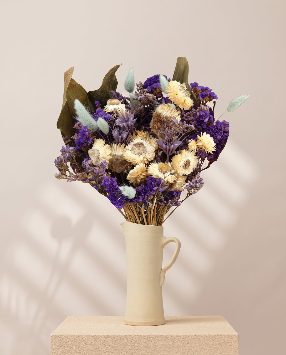 Ramo de flores secas em azul numa jarra de cerâmica creme. Jarra não incluída.