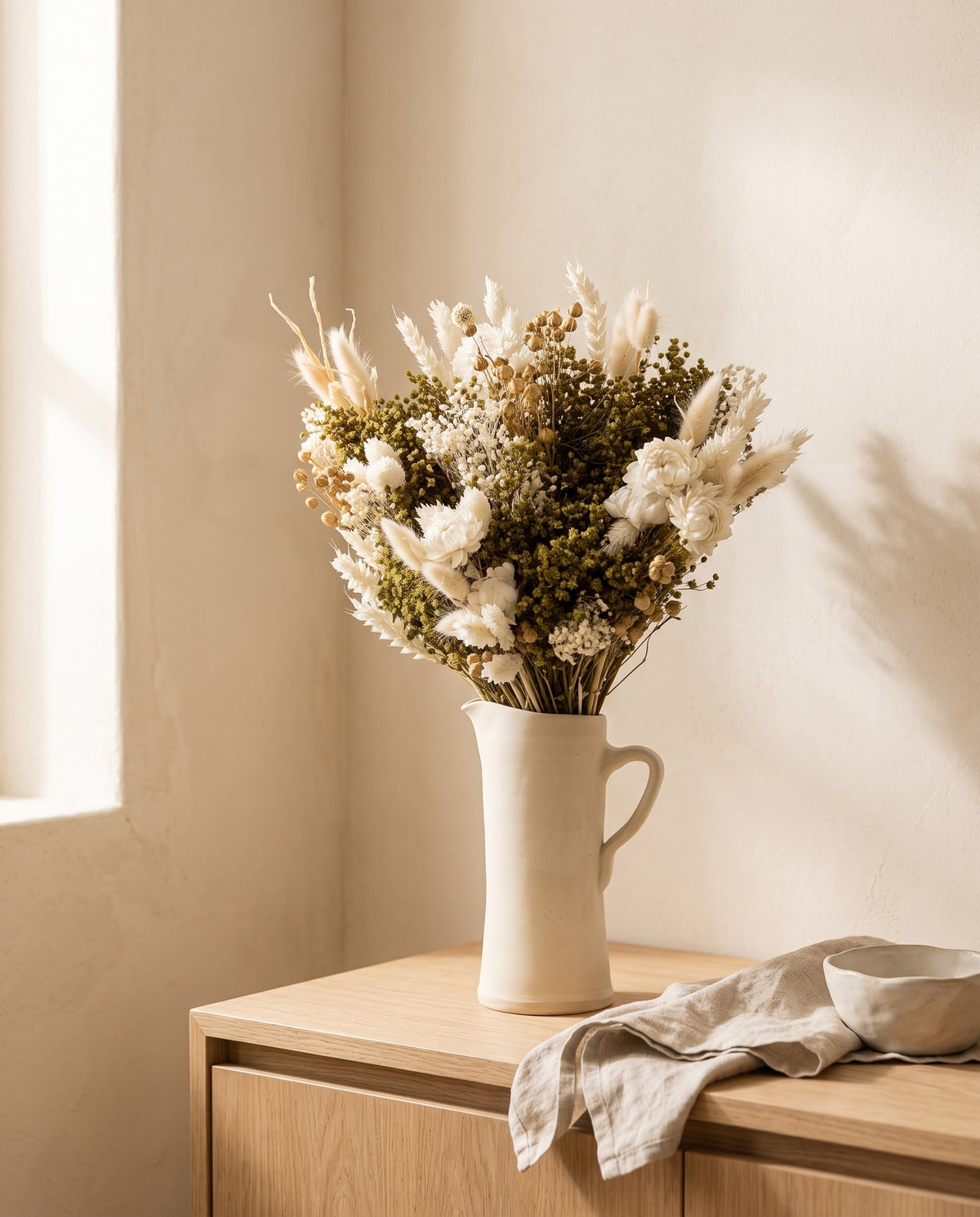 Ramo de flores secas em branco numa jarra sobre um aparador, ambiente de casa. Jarra não incluída.