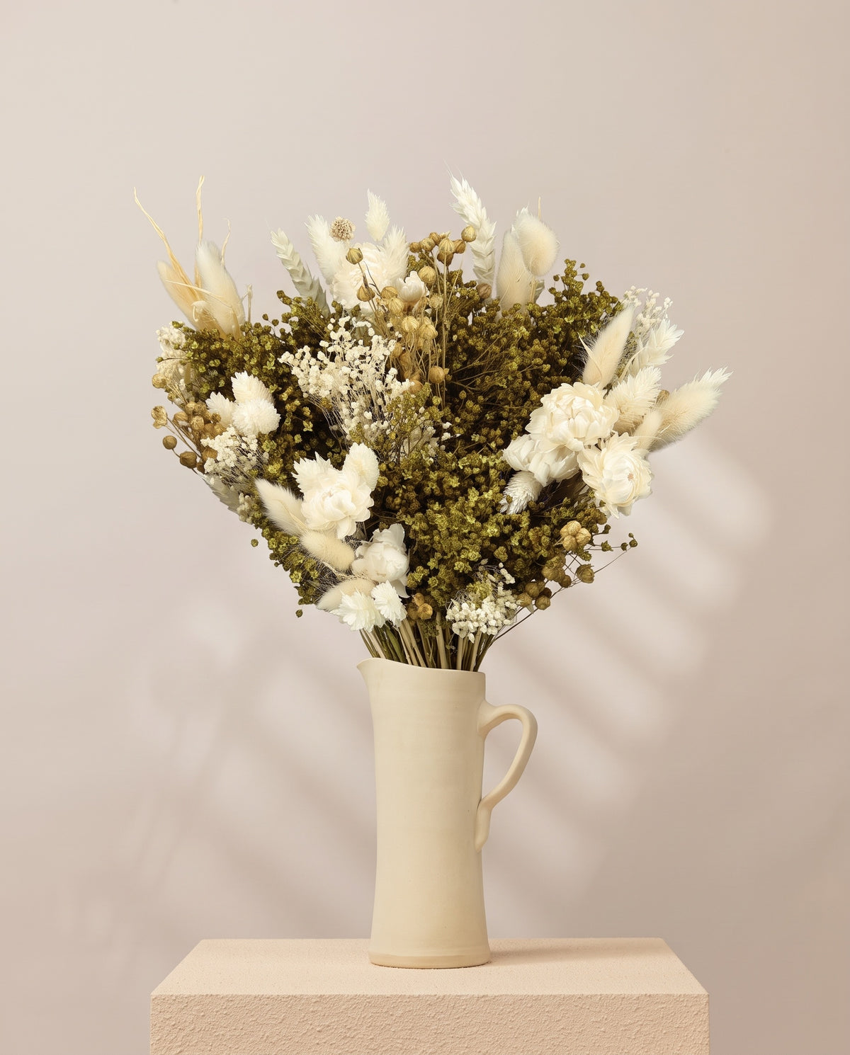 Ramo de flores secas em branco numa jarra de cerâmica creme. Jarra não incluída.