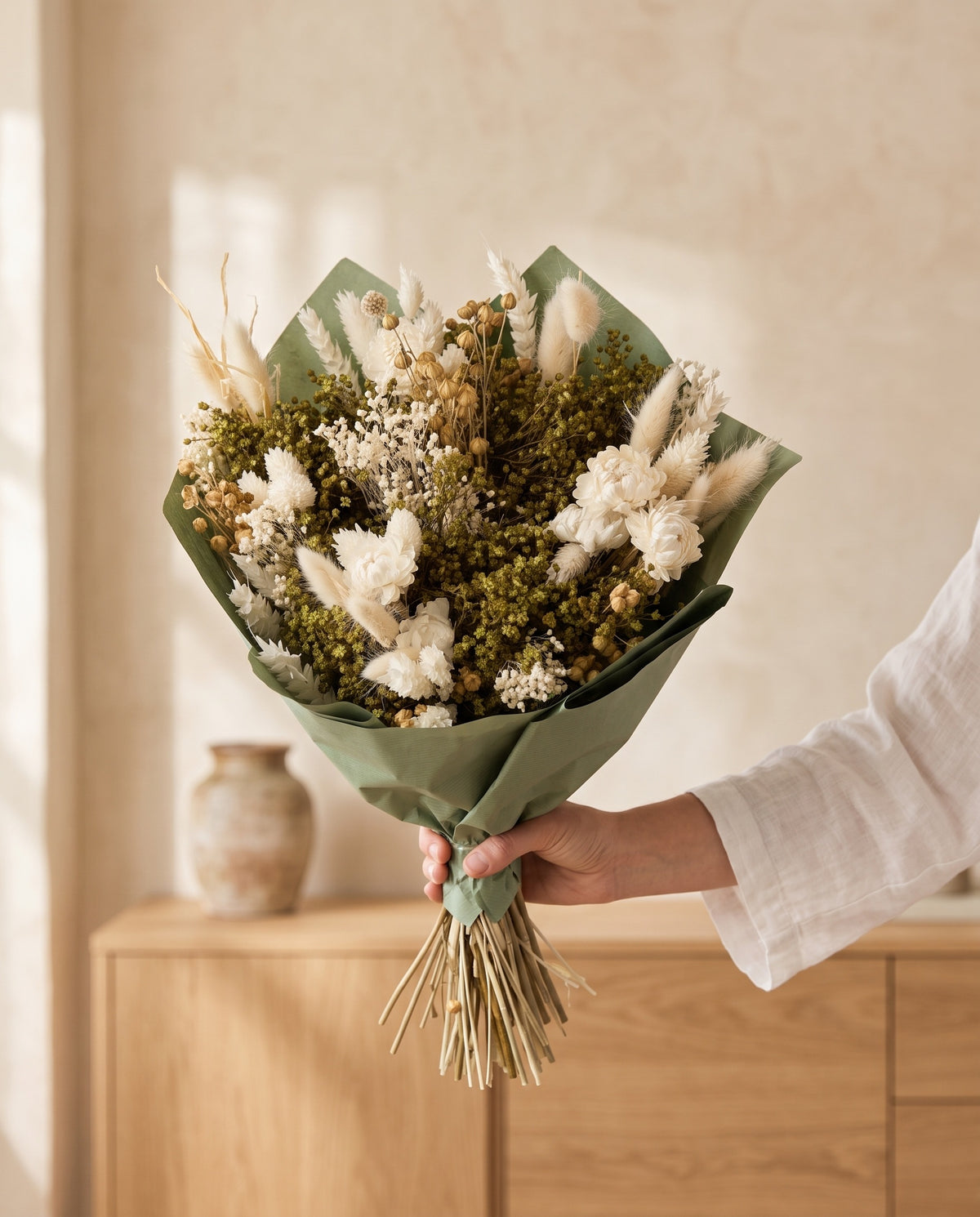 Mão a segurar o ramo de flores secas em branco com o seu papel, tal como é entregue.