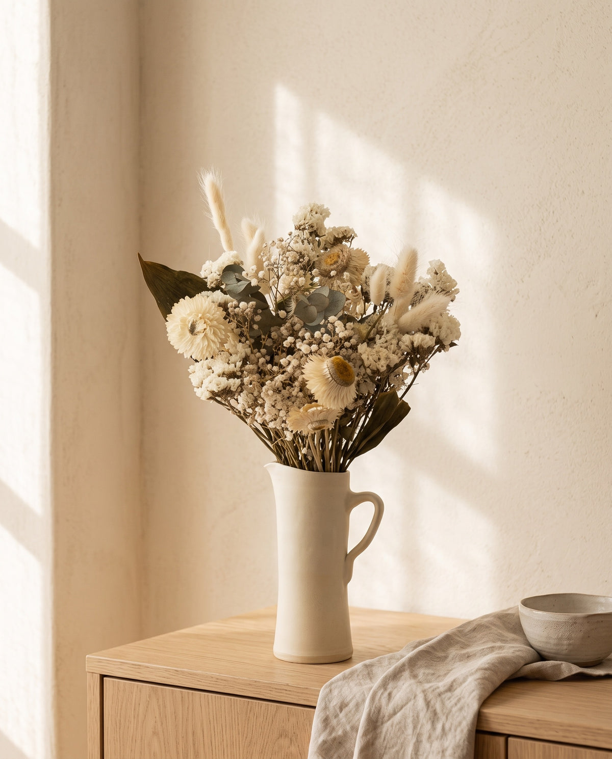 Ramo de flores secas em branco numa jarra sobre um aparador, ambiente de casa. Jarra não incluída.