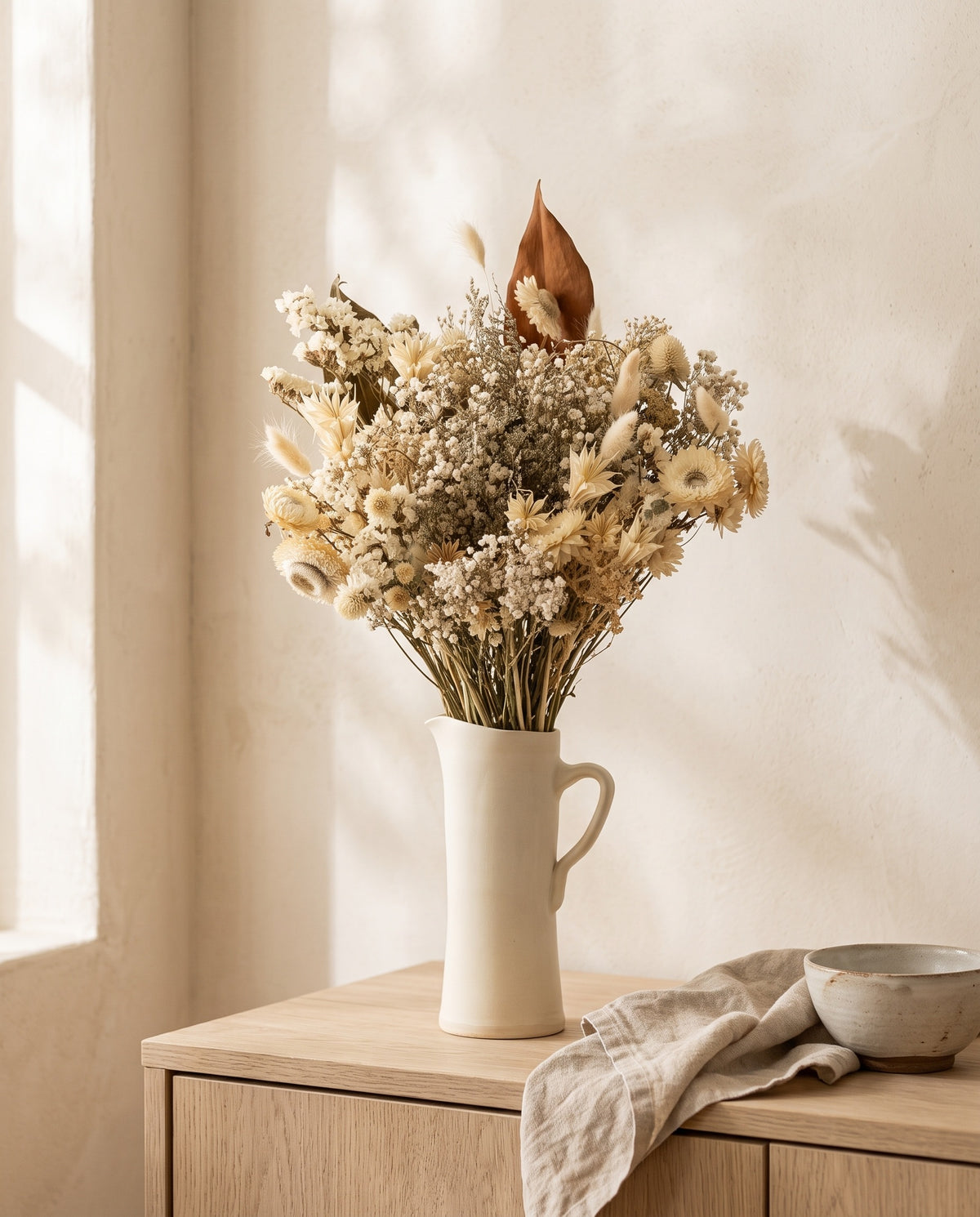 Ramo grande de flores secas em branco numa jarra sobre um aparador, ambiente de casa. Jarra não incluída.