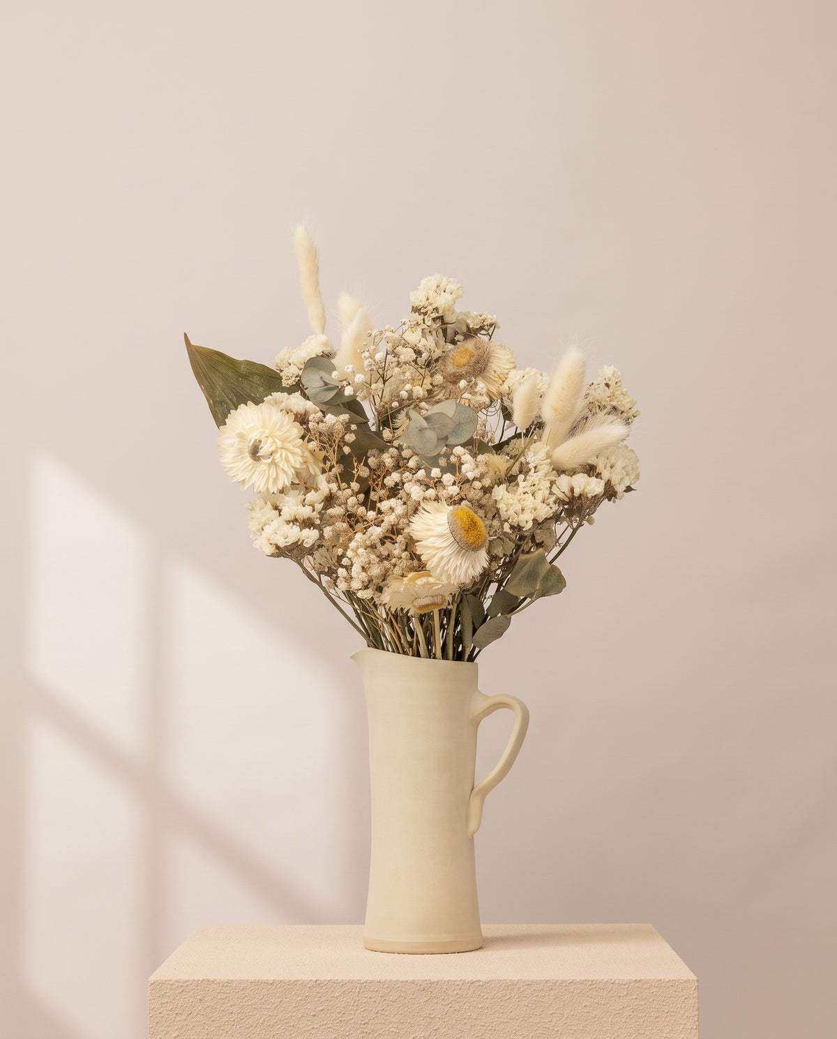 Ramo de flores secas em branco numa jarra de cerâmica creme. Jarra não incluída.