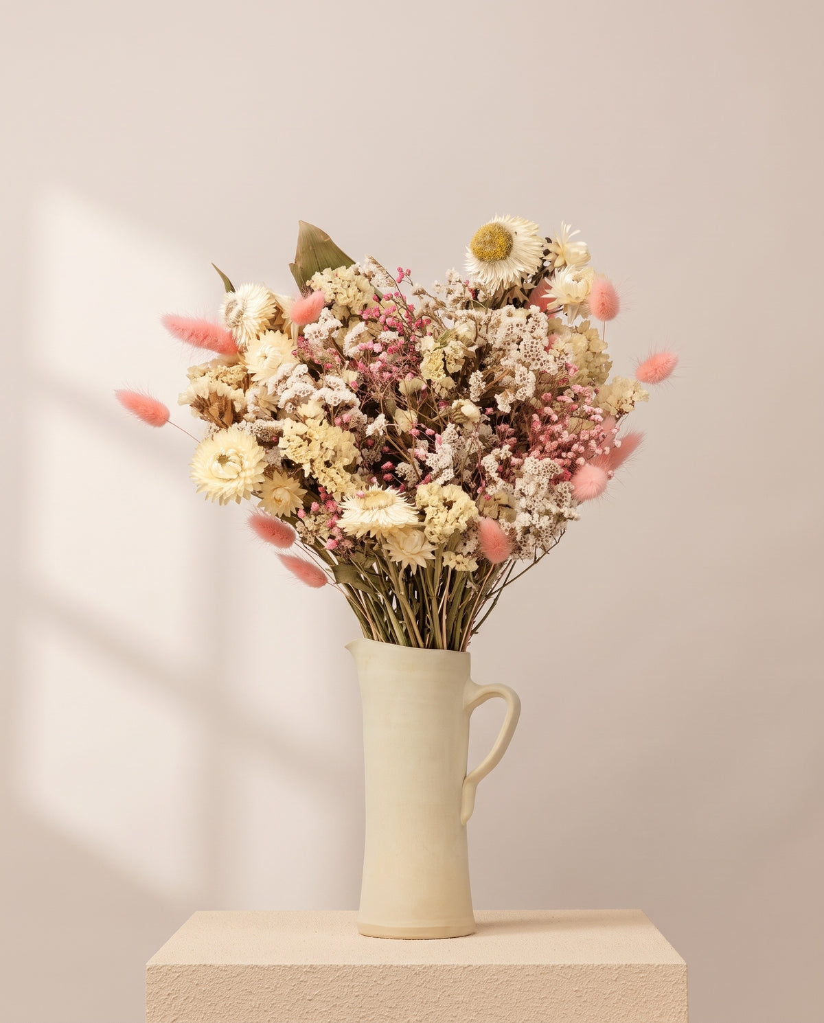 Ramo de flores secas en blanco y rosa en una jarra de cerámica crema. Jarra no incluida.