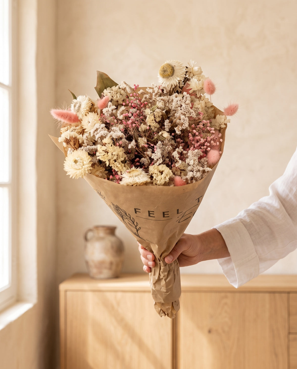 Mano sujetando el ramo de flores secas en blanco y rosa con su papel, como se entrega.