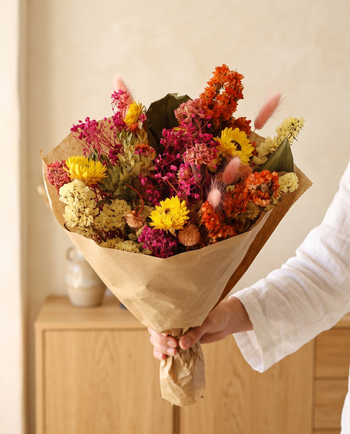 Mão a segurar o ramo de flores secas multicolor com o seu papel, tal como é entregue.