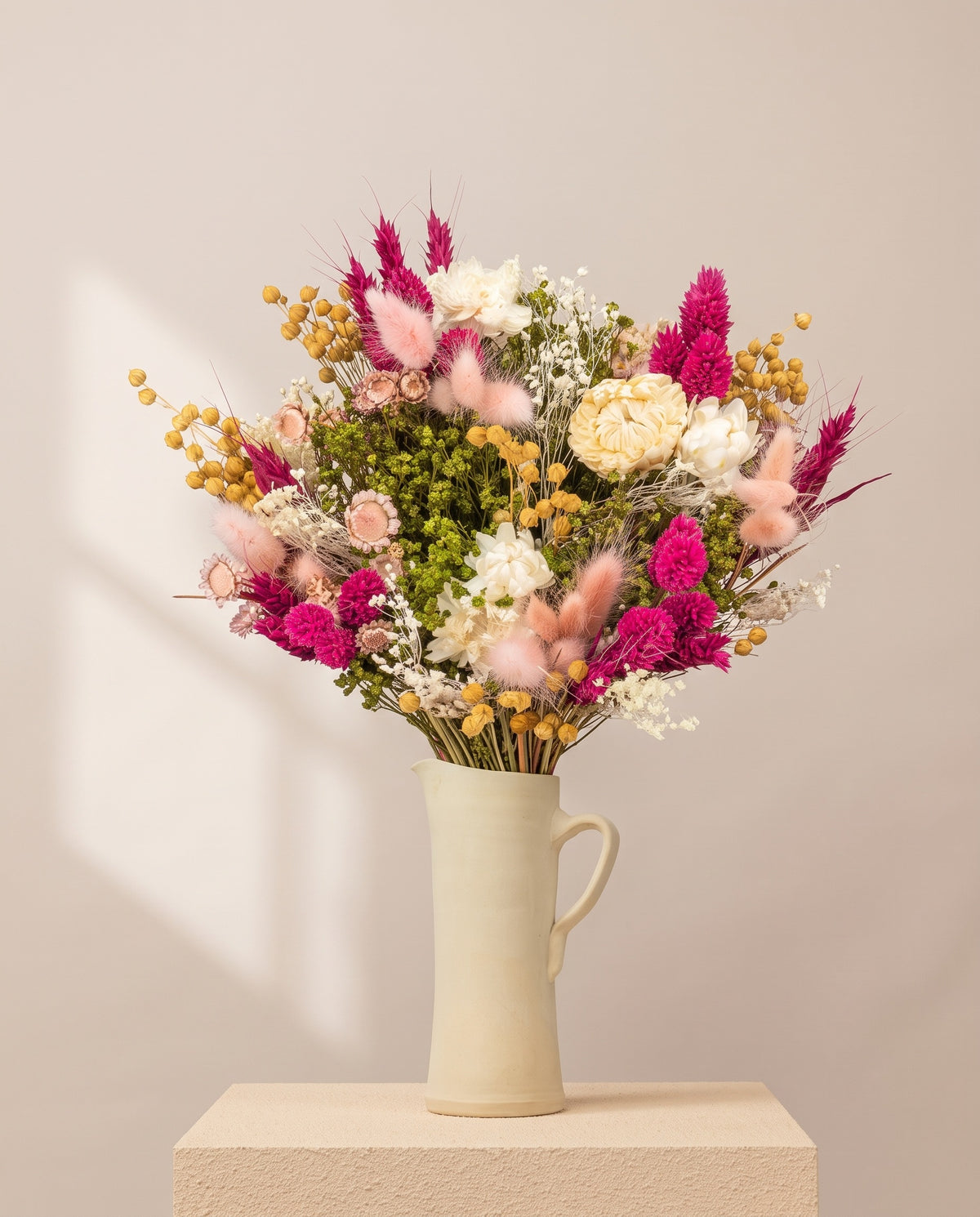 Ramo de flores secas em fúcsia com phalaris numa jarra de cerâmica creme. Jarra não incluída.