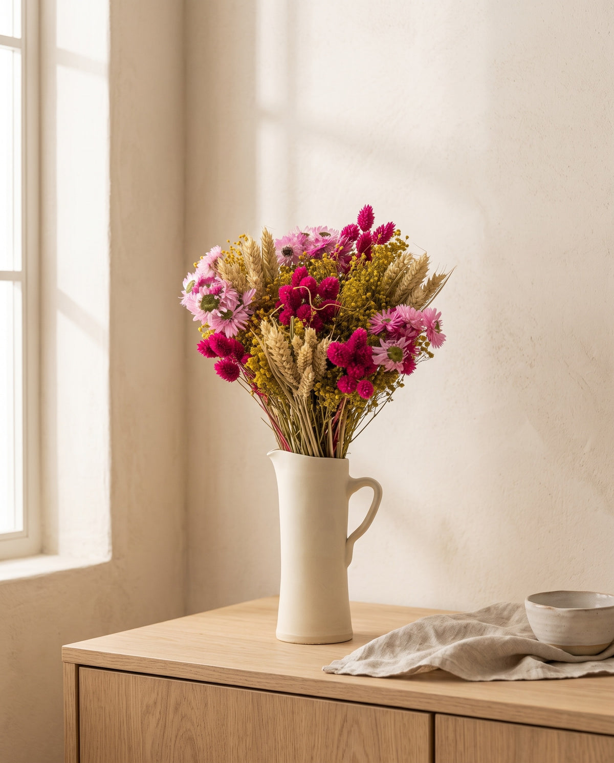 Ramo de flores secas em fúcsia com trigo numa jarra sobre um aparador, ambiente de casa. Jarra não incluída.