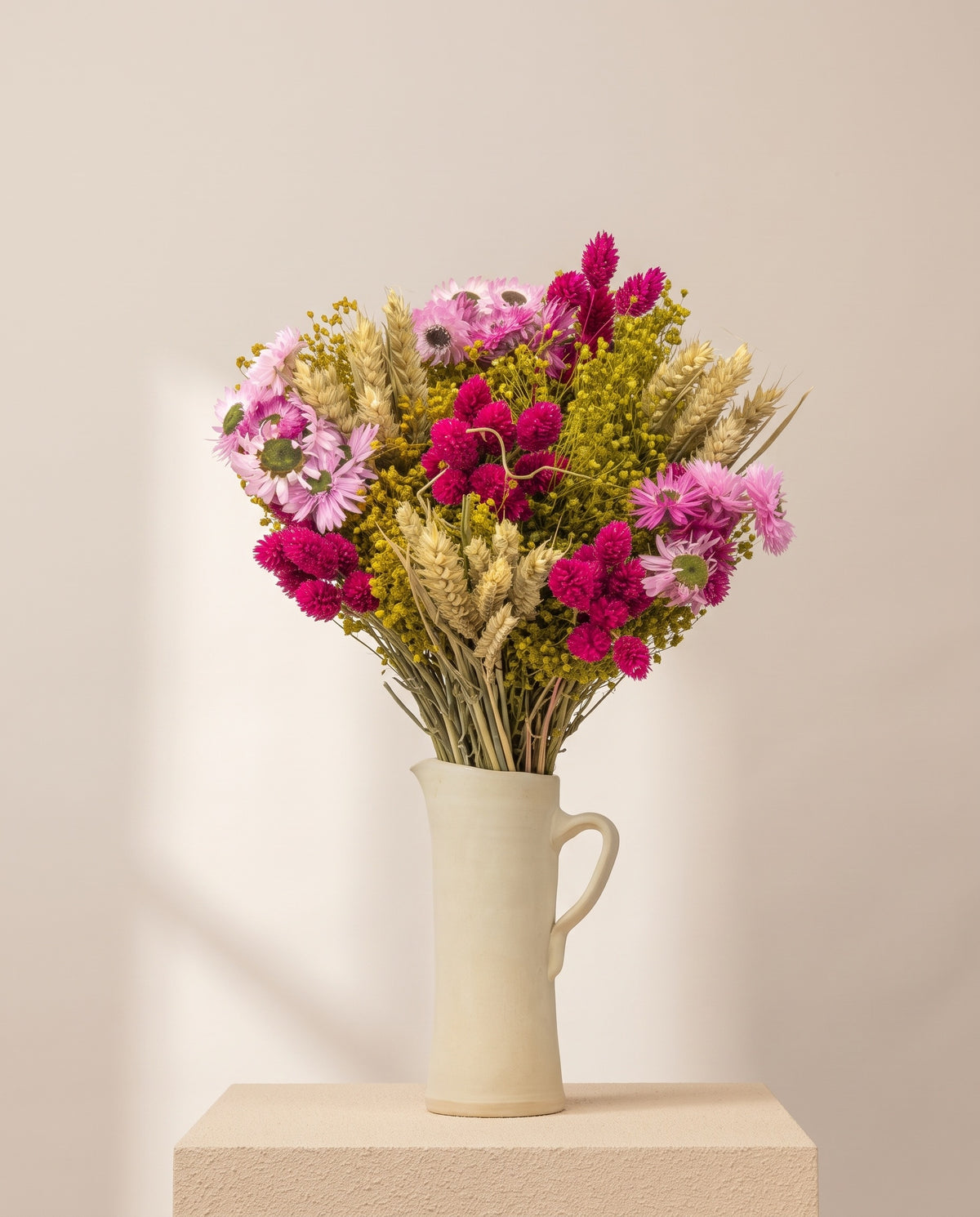 Ramo de flores secas em fúcsia com trigo numa jarra de cerâmica creme. Jarra não incluída.