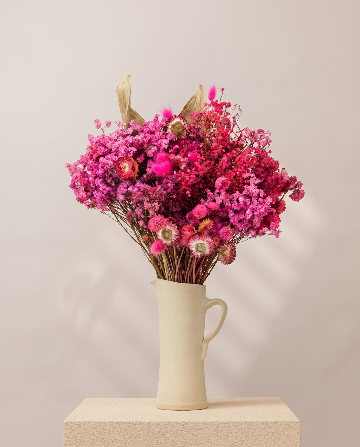 Ramo grande de flores secas en fucsia en una jarra de cerámica crema. Jarra no incluida.