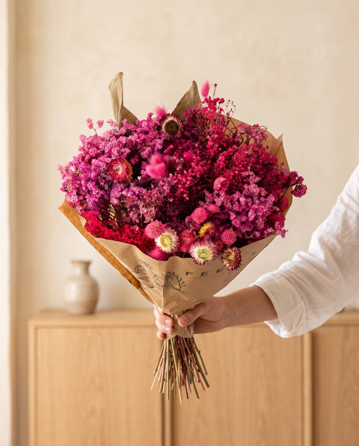 Mano sujetando el ramo grande de flores secas en fucsia con su papel, como se entrega.