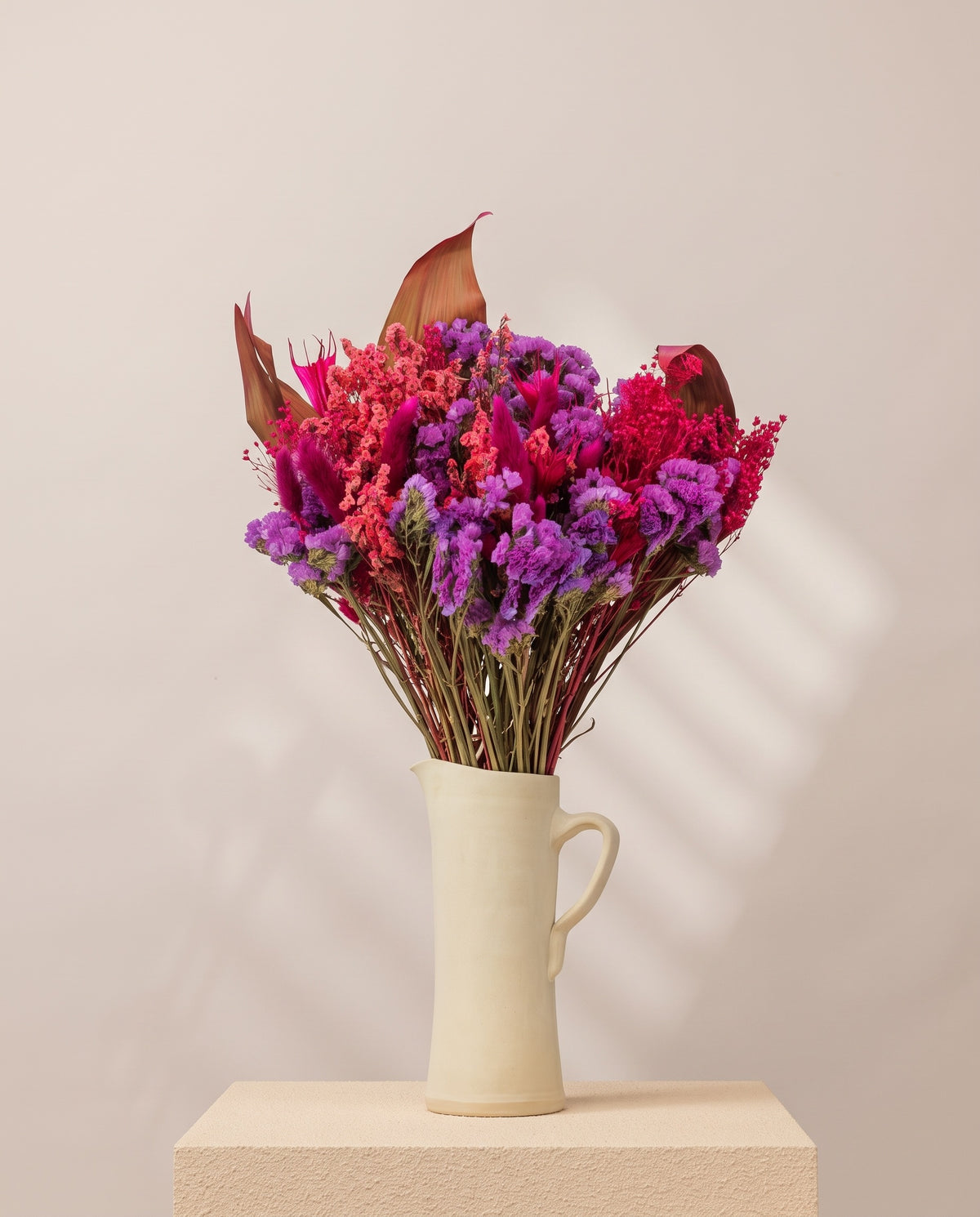 Ramo de flores secas em fúcsia numa jarra de cerâmica creme. Jarra não incluída.