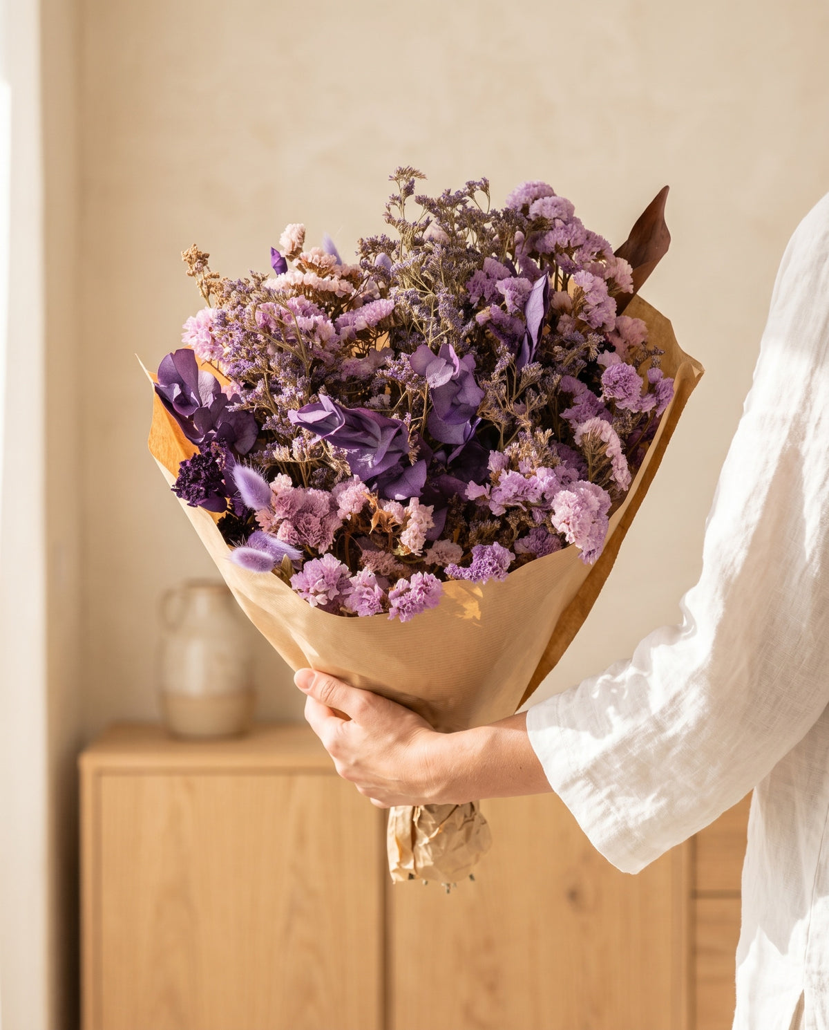 Mão a segurar o ramo grande de flores secas em lavanda com o seu papel, tal como é entregue.