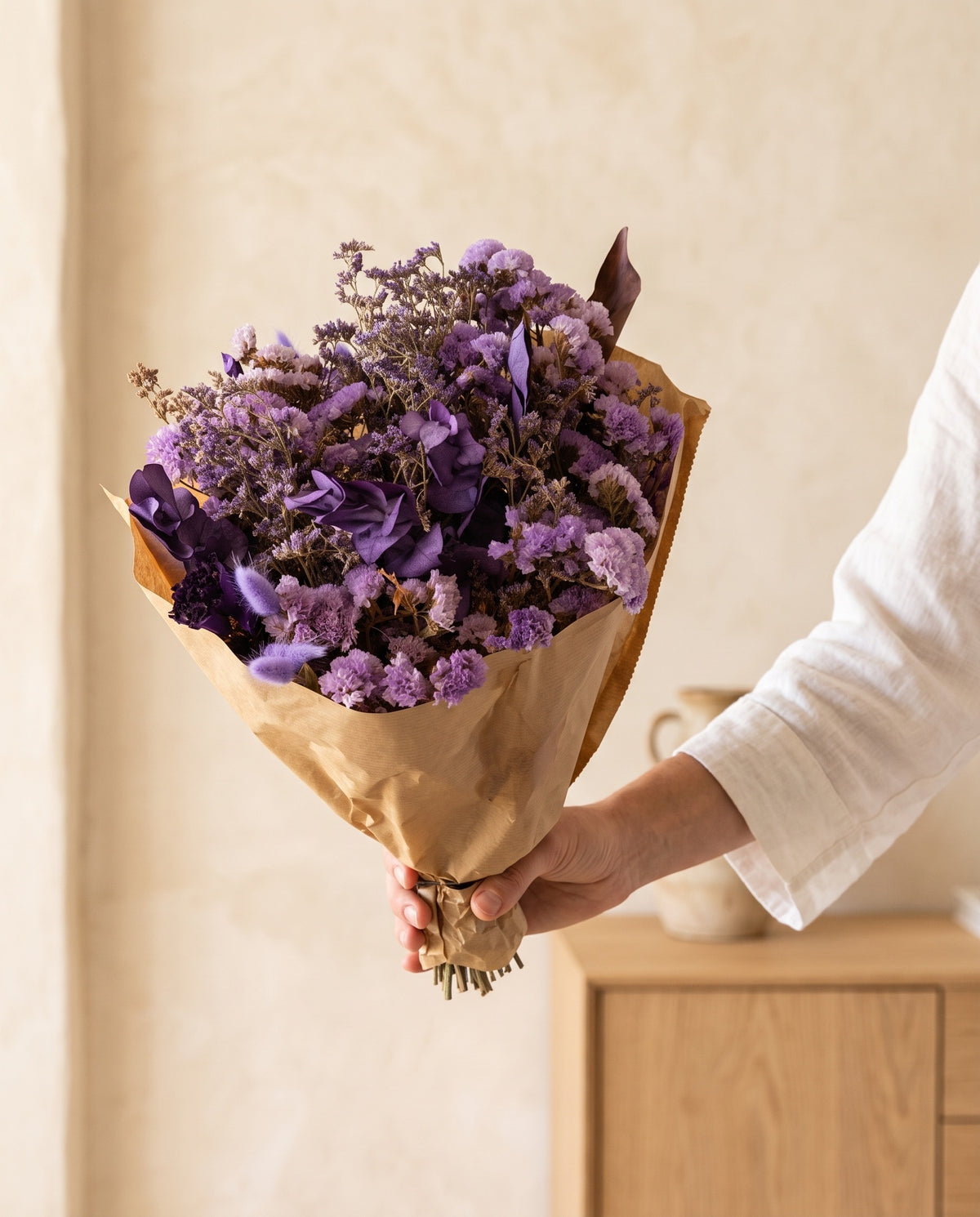 Mão a segurar o ramo de flores secas em lavanda com o seu papel, tal como é entregue.