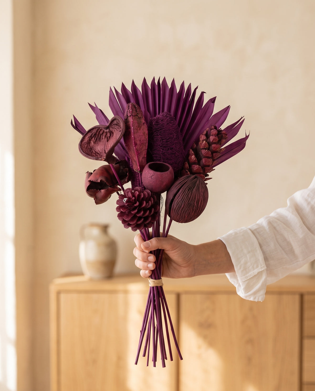 Mano sujetando el ramo de flores secas en morado con piñas, para ver su tamaño.