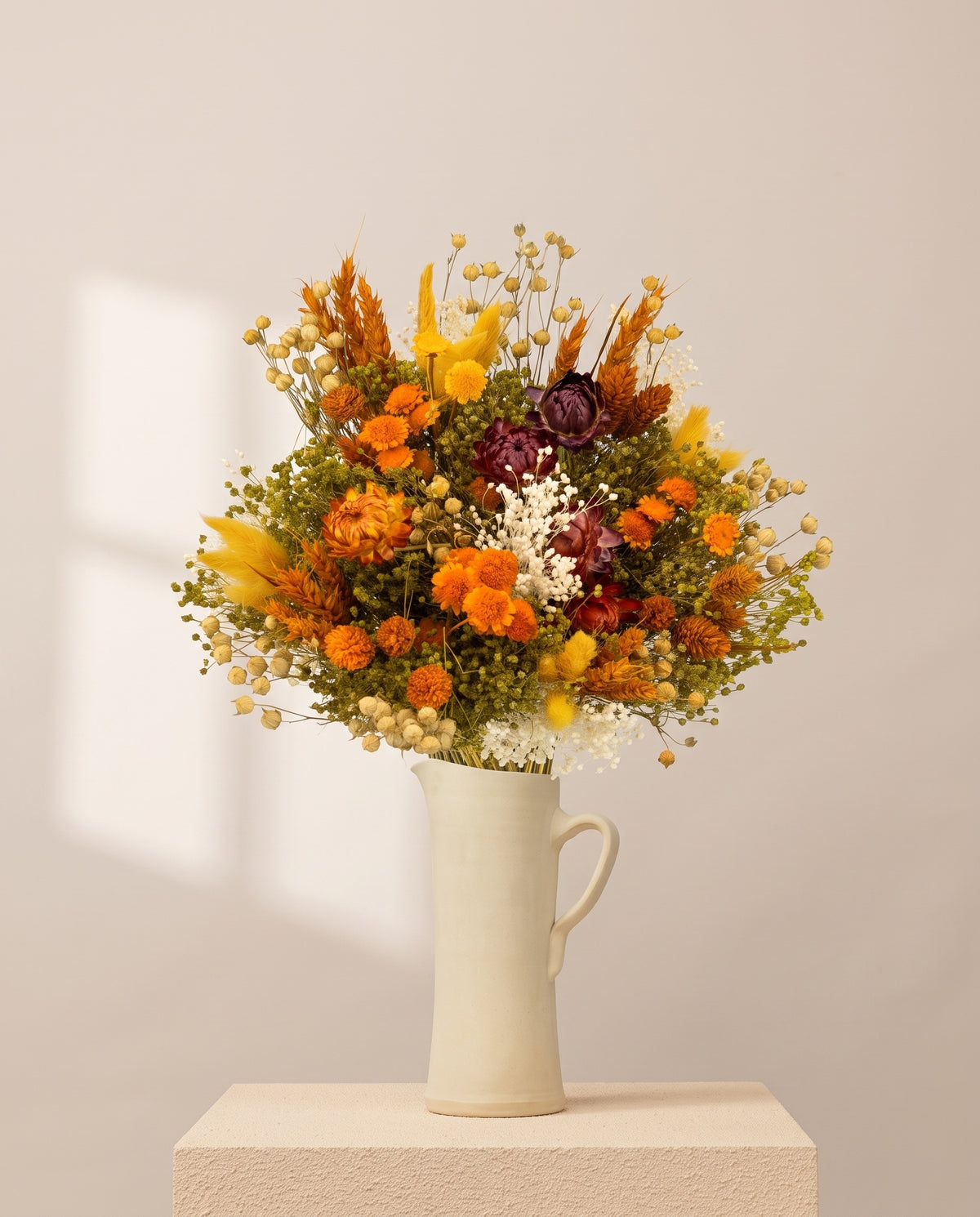 Ramo de flores secas em laranja com helichrysum numa jarra de cerâmica creme. Jarra não incluída.