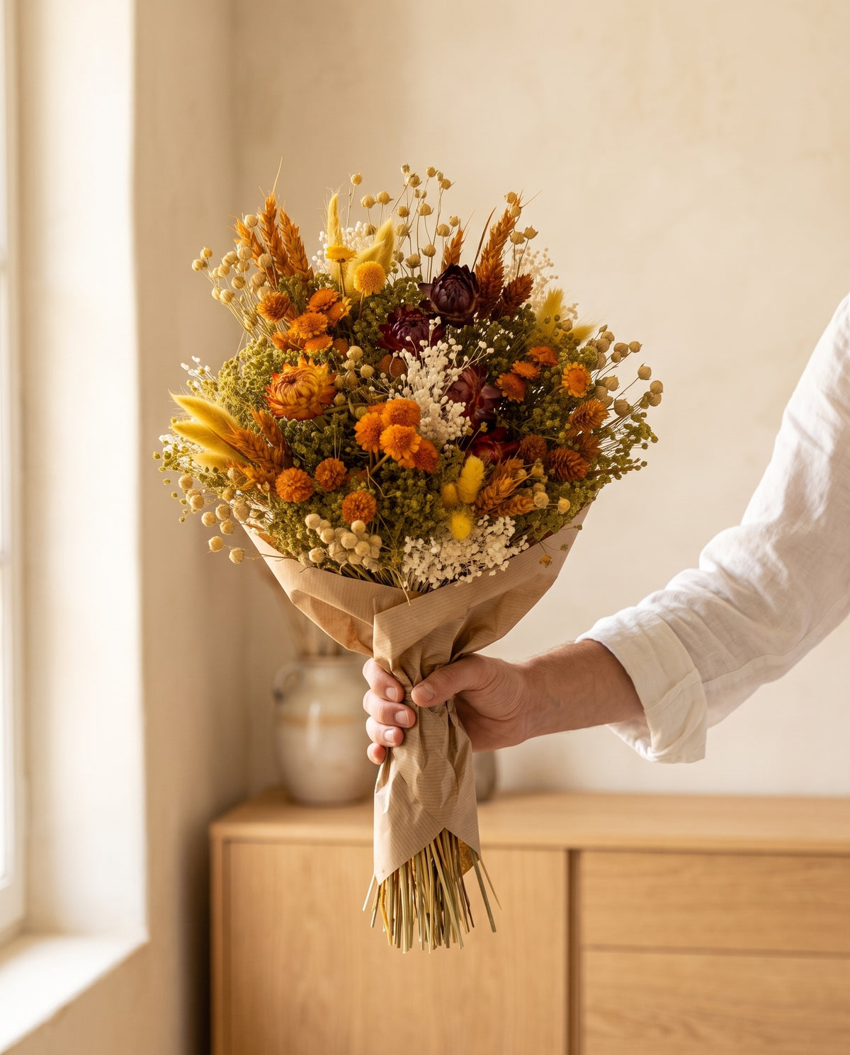 Mão a segurar o ramo de flores secas em laranja com helichrysum com o seu papel, tal como é entregue.