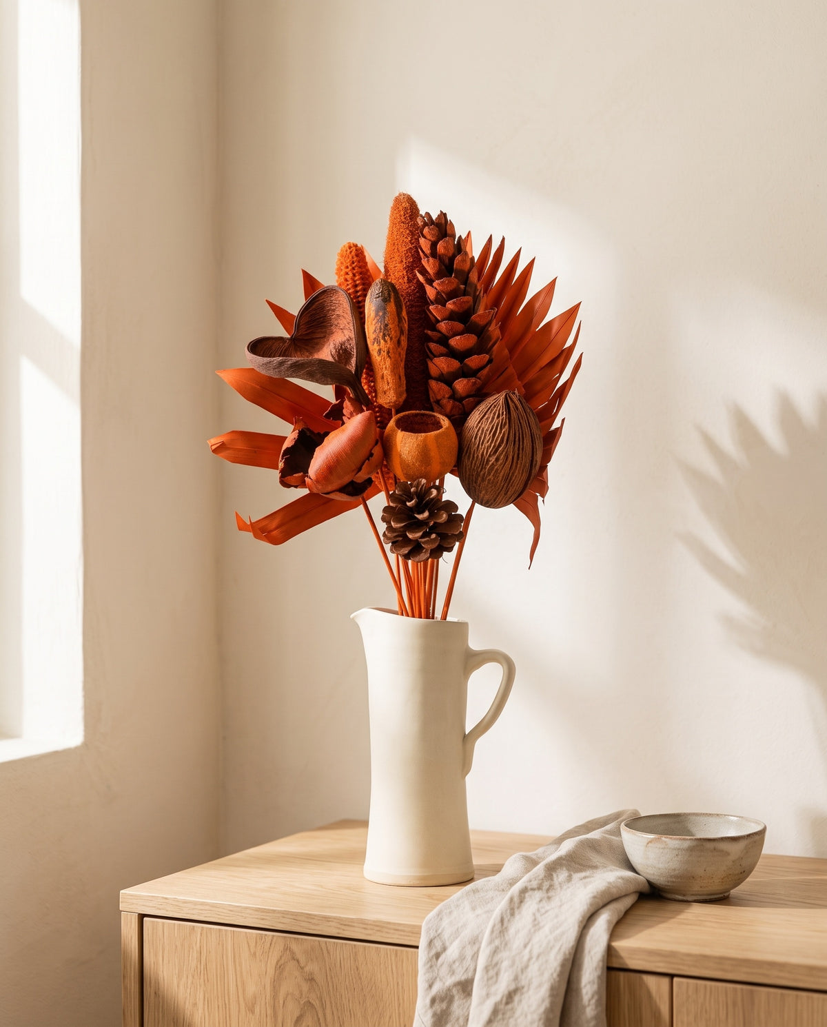 Ramo de flores secas em laranja com pinhas numa jarra sobre um aparador, ambiente de casa. Jarra não incluída.