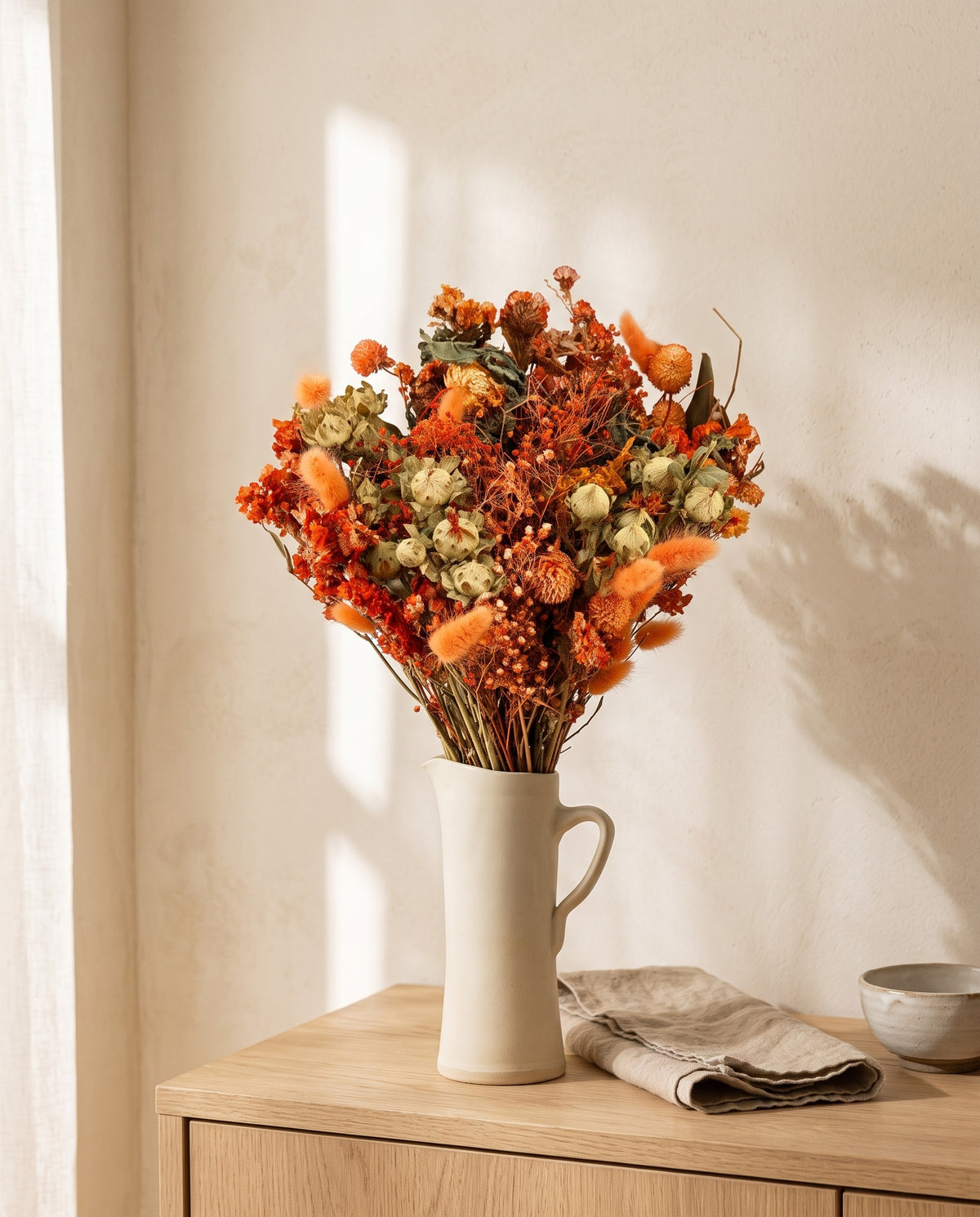 Ramo de flores secas em laranja numa jarra sobre um aparador, ambiente de casa. Jarra não incluída.