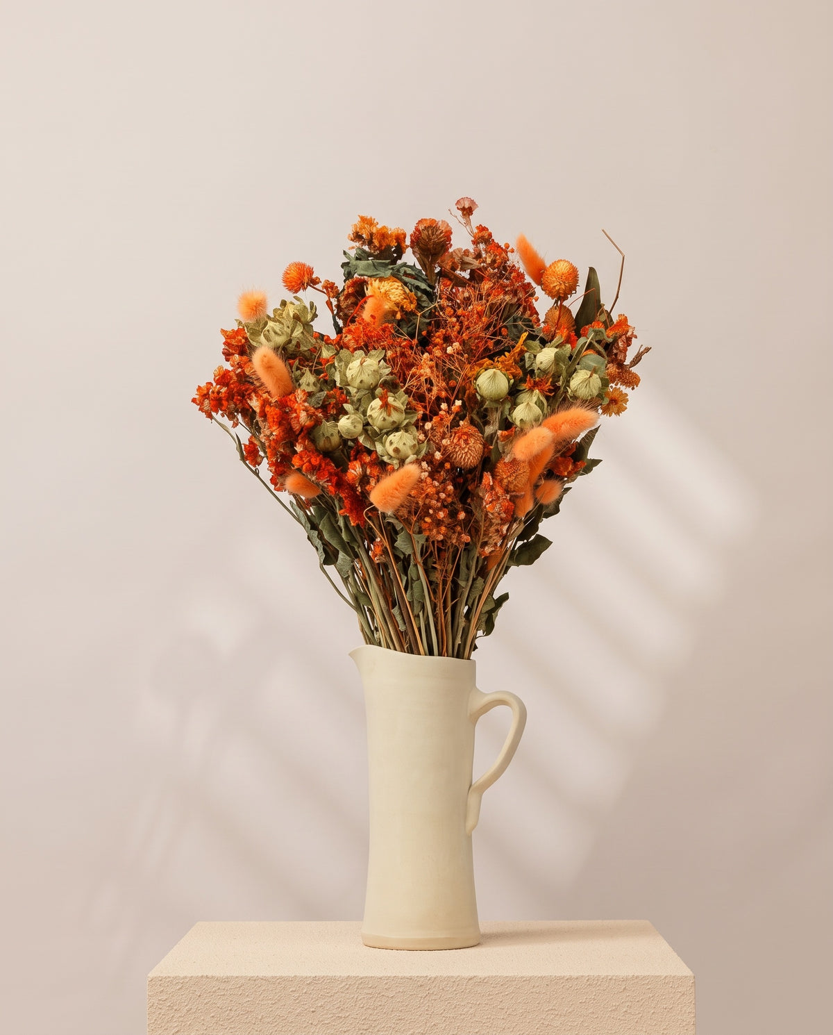 Ramo de flores secas em laranja numa jarra de cerâmica creme. Jarra não incluída.