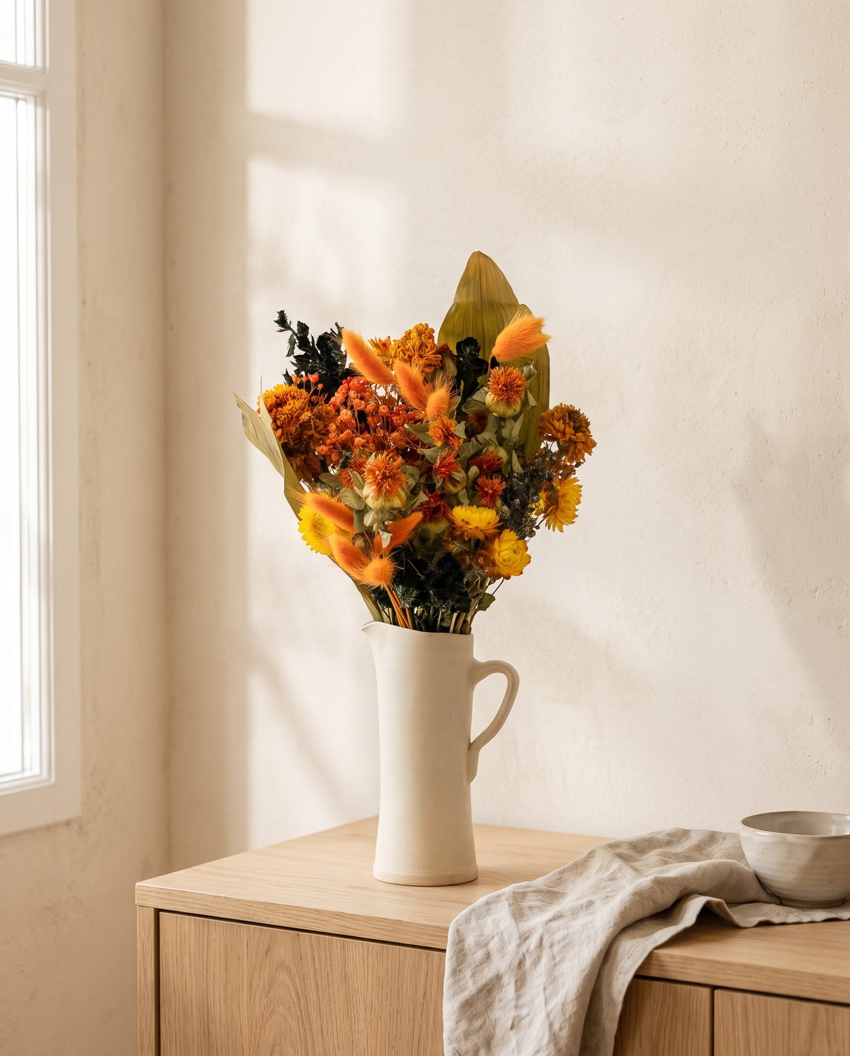Ramo de flores secas em laranja e preto numa jarra sobre um aparador, ambiente de casa. Jarra não incluída.