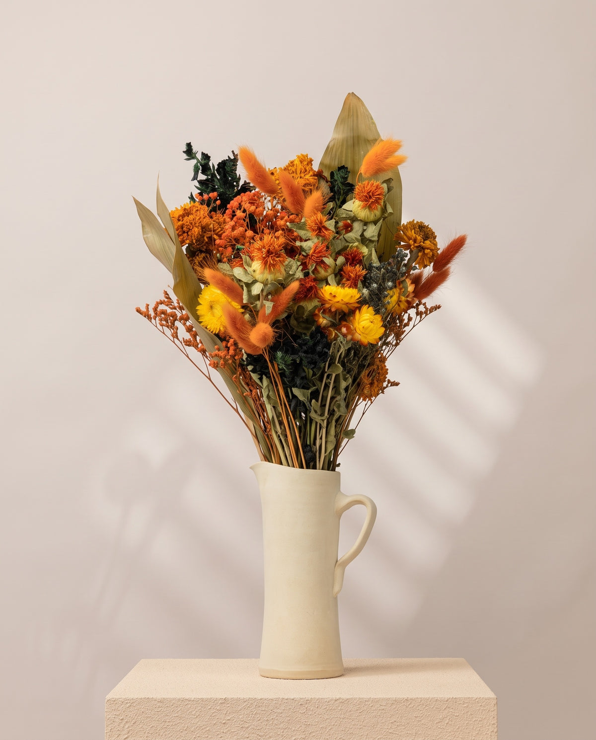 Ramo de flores secas em laranja e preto numa jarra de cerâmica creme. Jarra não incluída.