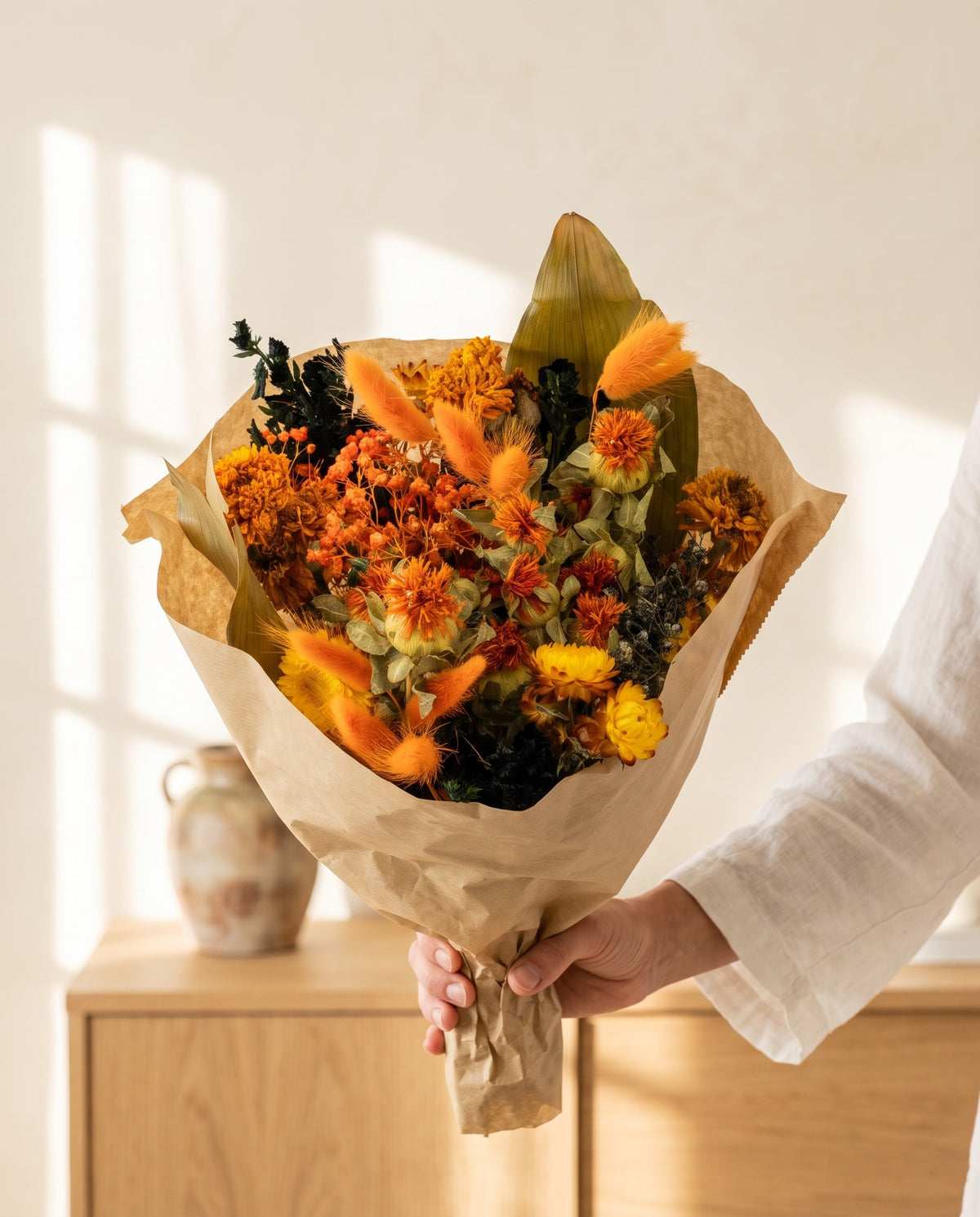 Mão a segurar o ramo de flores secas em laranja e preto com o seu papel, tal como é entregue.
