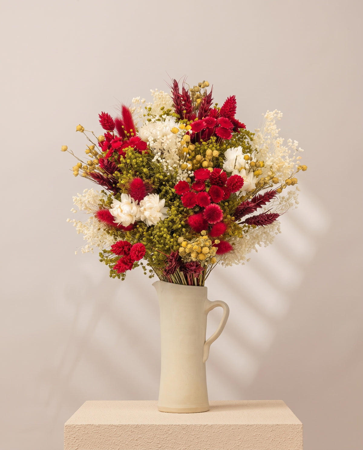 Ramo de flores secas em vermelho numa jarra de cerâmica creme. Jarra não incluída.