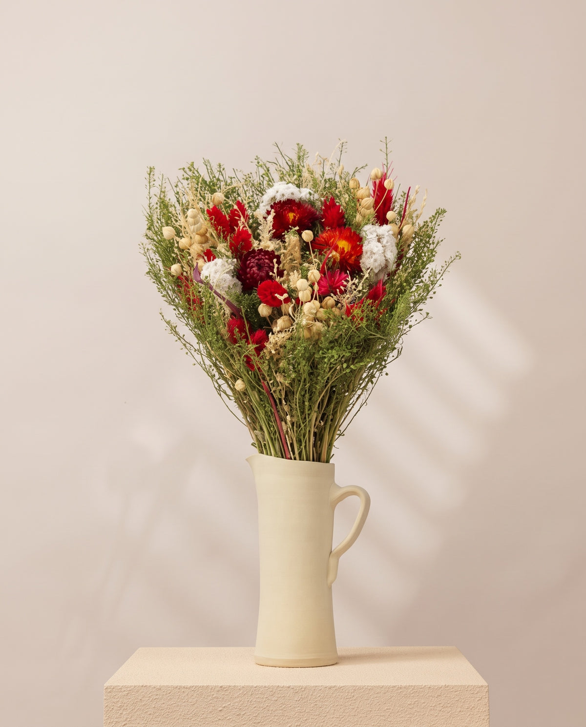 Ramo de flores secas em vermelho numa jarra de cerâmica creme. Jarra não incluída.