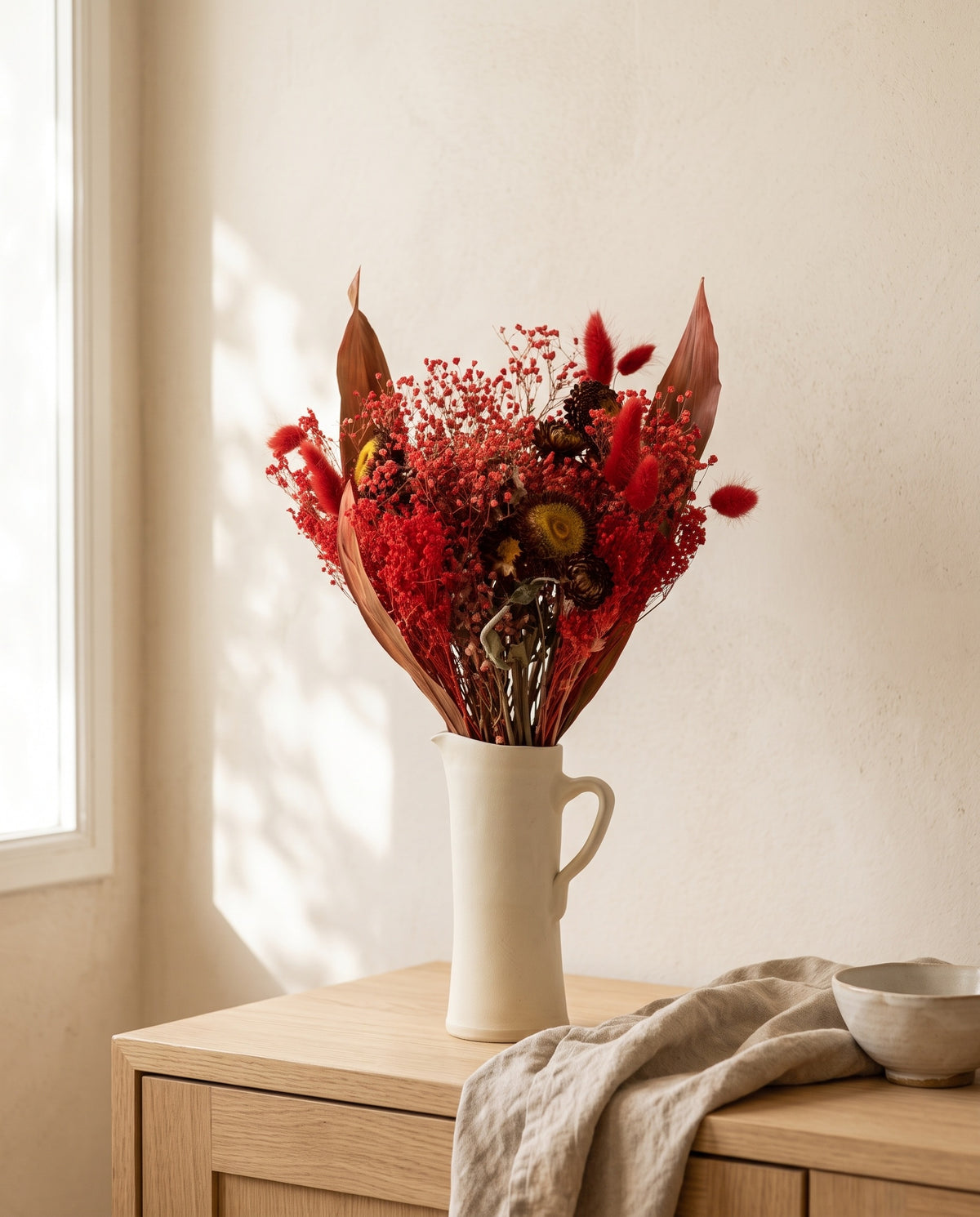 Ramo de flores secas en rojo en una jarra sobre un aparador, ambiente de casa. Jarra no incluida.