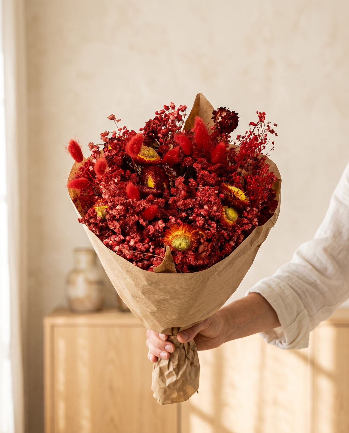 Mano sujetando el ramo grande de flores secas en rojo con su papel, como se entrega.