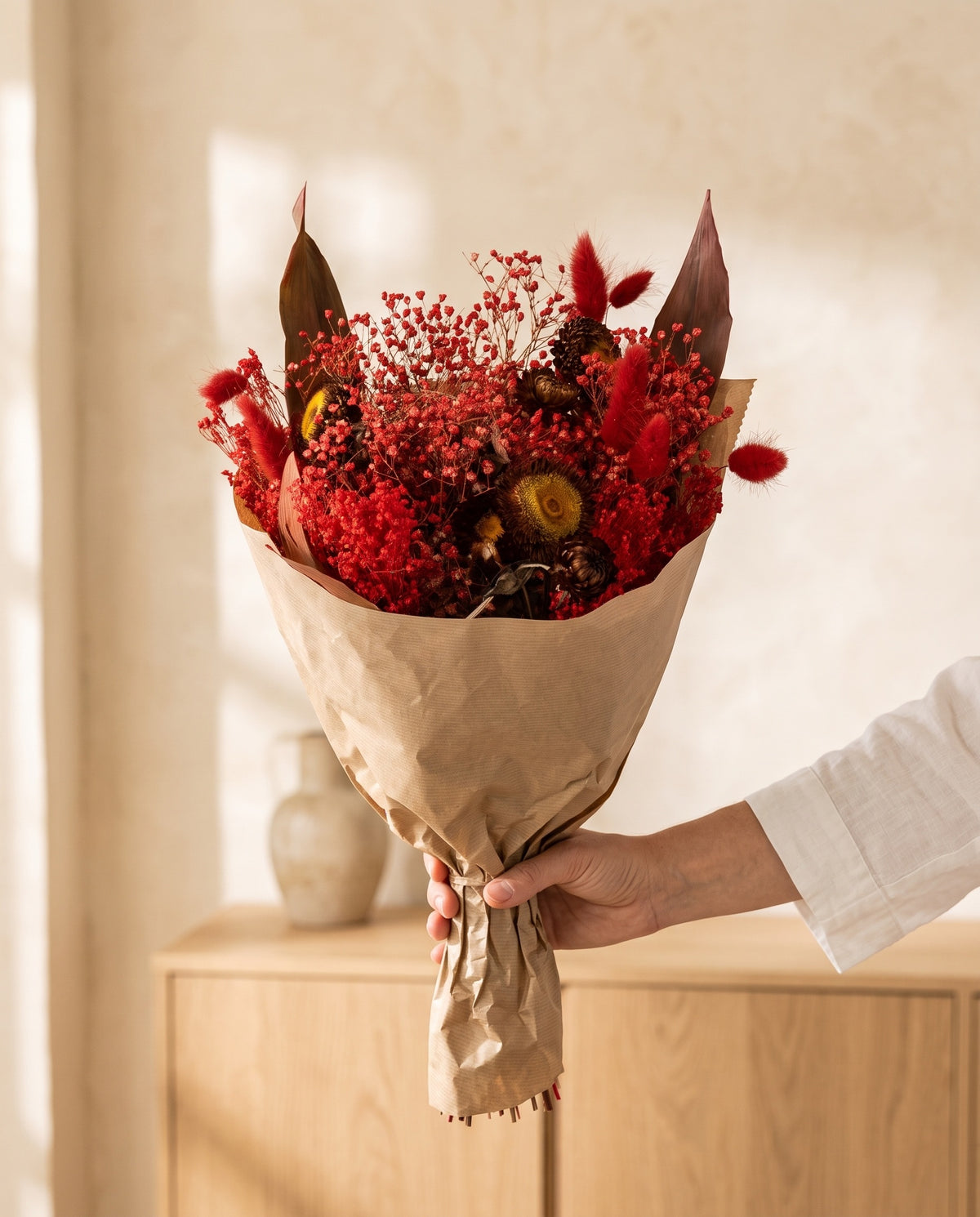 Mano sujetando el ramo de flores secas en rojo con su papel, como se entrega.