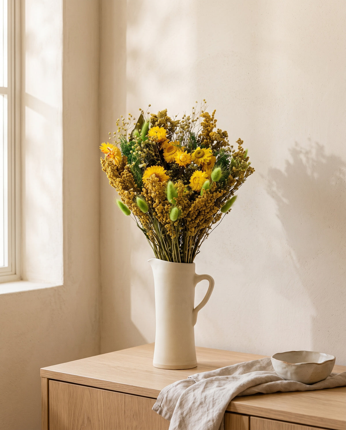 Ramo de flores secas em verde e amarelo numa jarra sobre um aparador, ambiente de casa. Jarra não incluída.