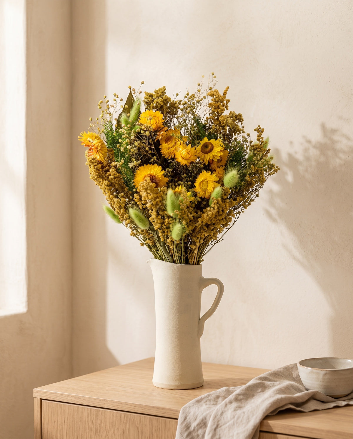 Ramo grande de flores secas em verde e amarelo numa jarra sobre um aparador, ambiente de casa. Jarra não incluída.