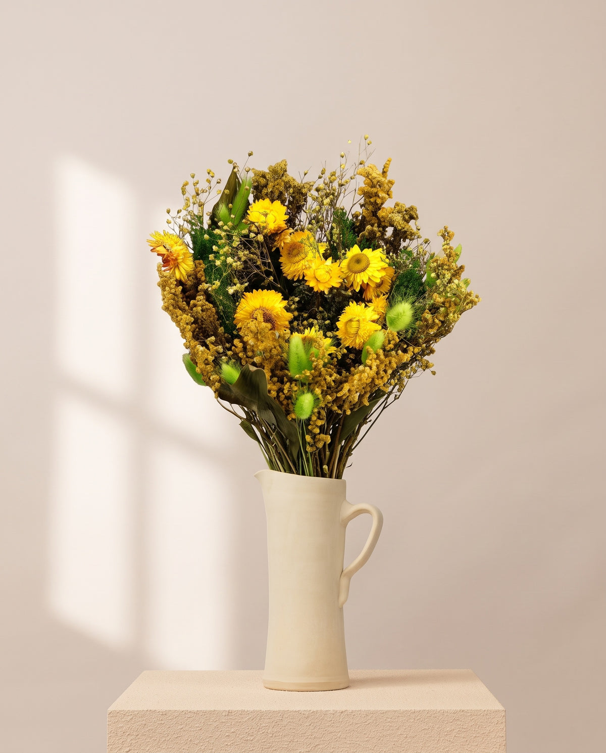 Ramo de flores secas em verde e amarelo numa jarra de cerâmica creme. Jarra não incluída.
